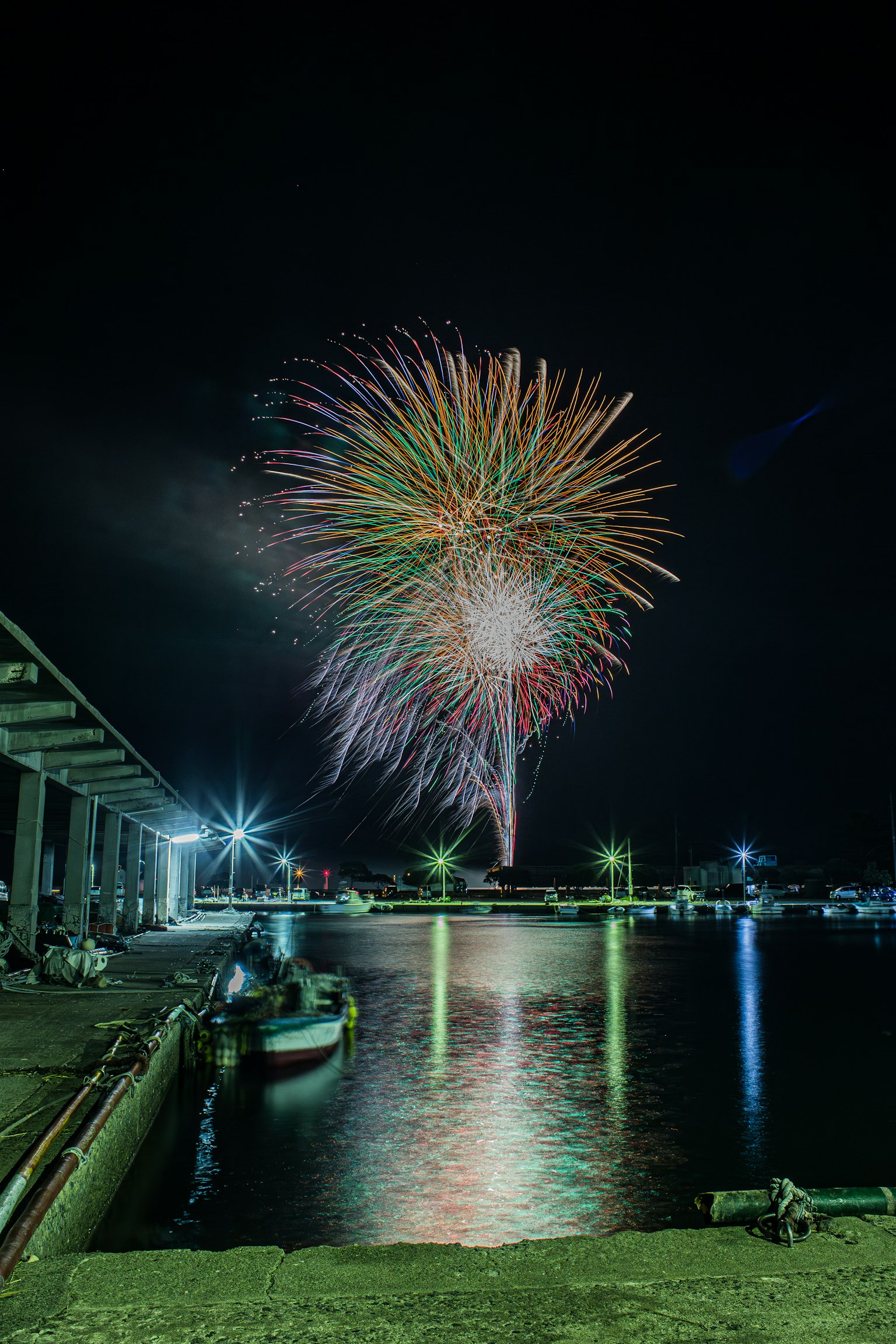 Fuegos artificiales coloridos estallando en el cielo nocturno sobre un puerto reflejándose en el agua