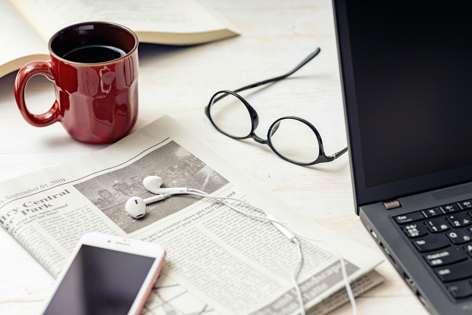 Eine rote Tasse und eine Zeitung auf einem Schreibtisch mit einem Laptop und einem Smartphone