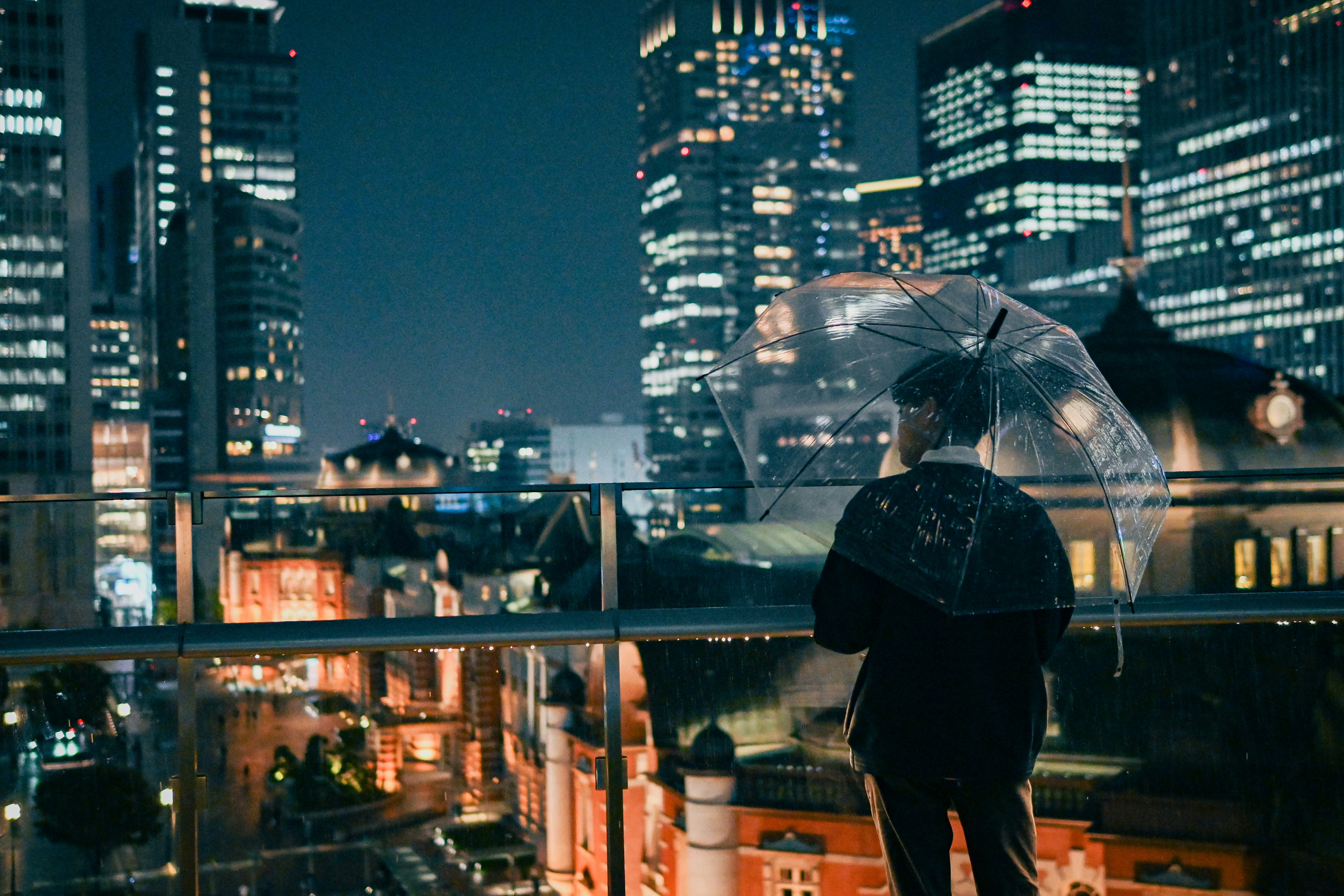 雨の夜に傘をさす人と高層ビルの夜景