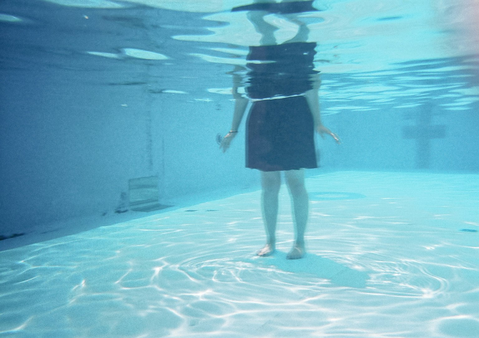 Una persona in piedi sott'acqua con riflessi sulla superficie d'acqua blu
