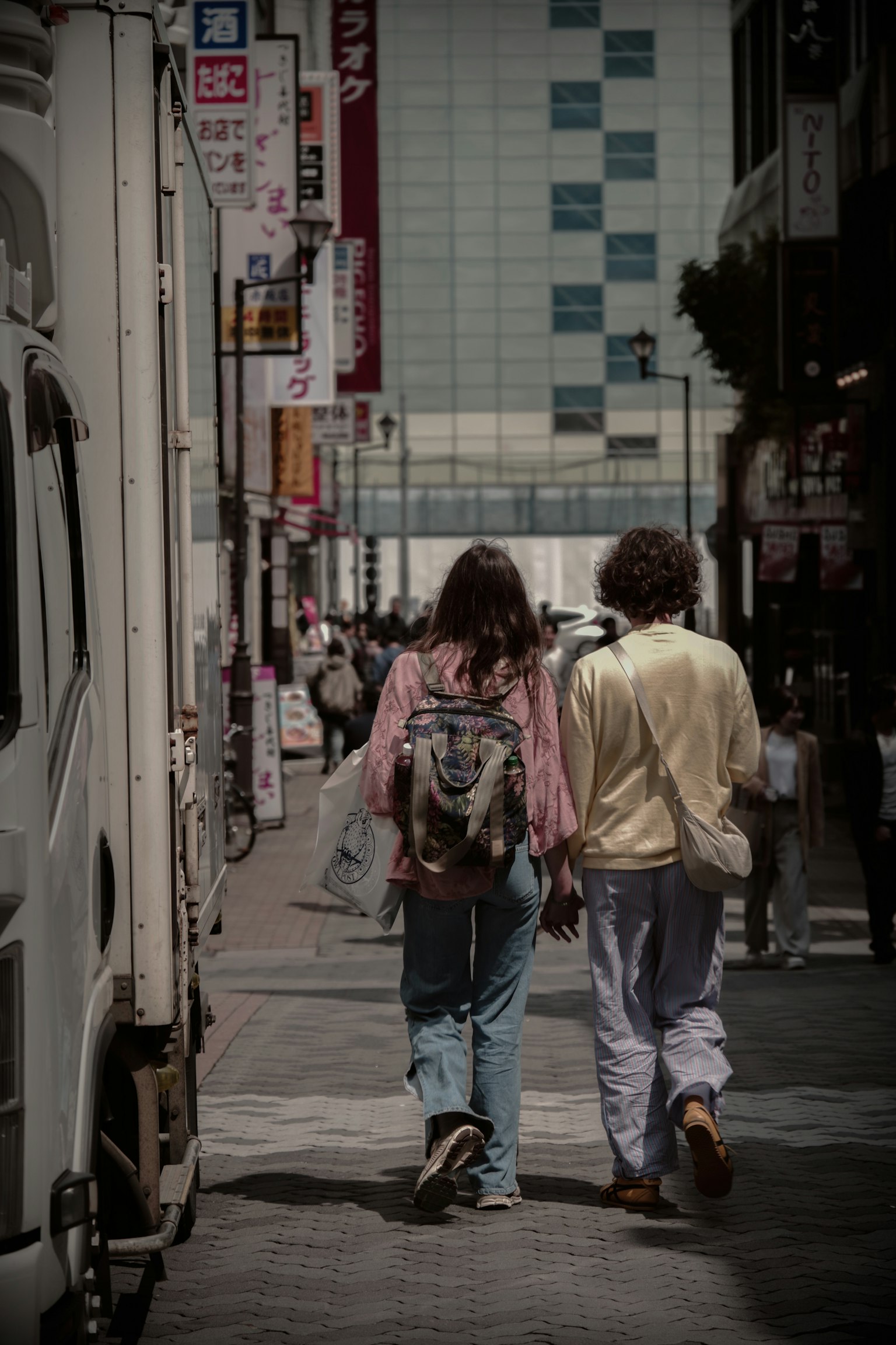 兩個年輕人在城市街道上背影行走，女性背著背包，男性穿著淺色衣服