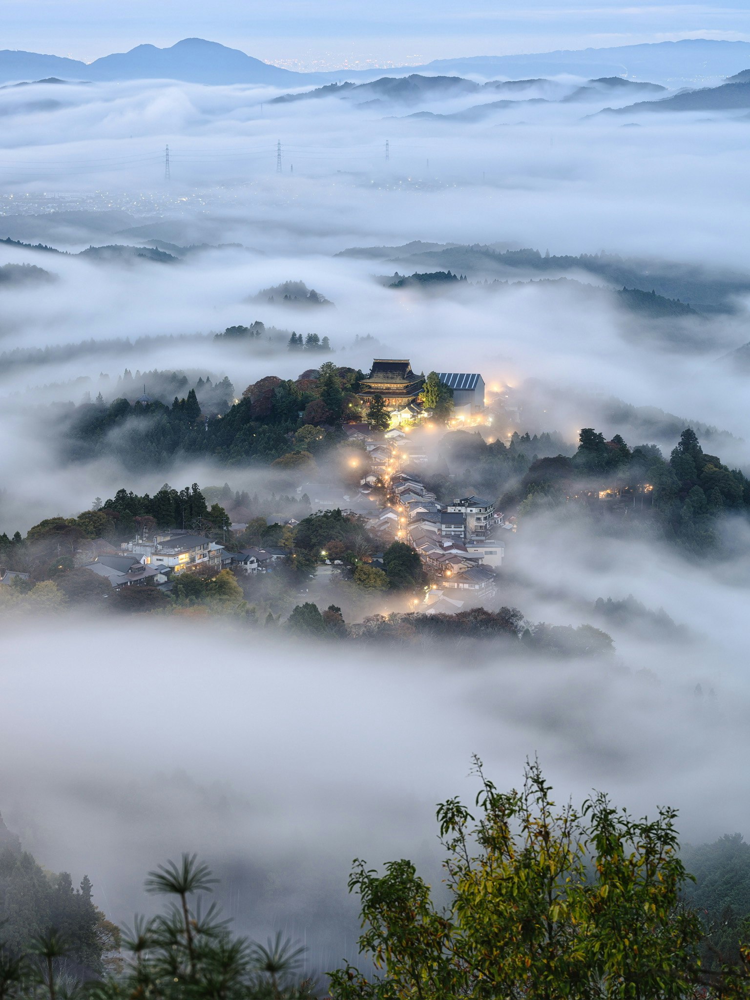一個被霧籠罩的山中村莊，夜晚散落的燈光