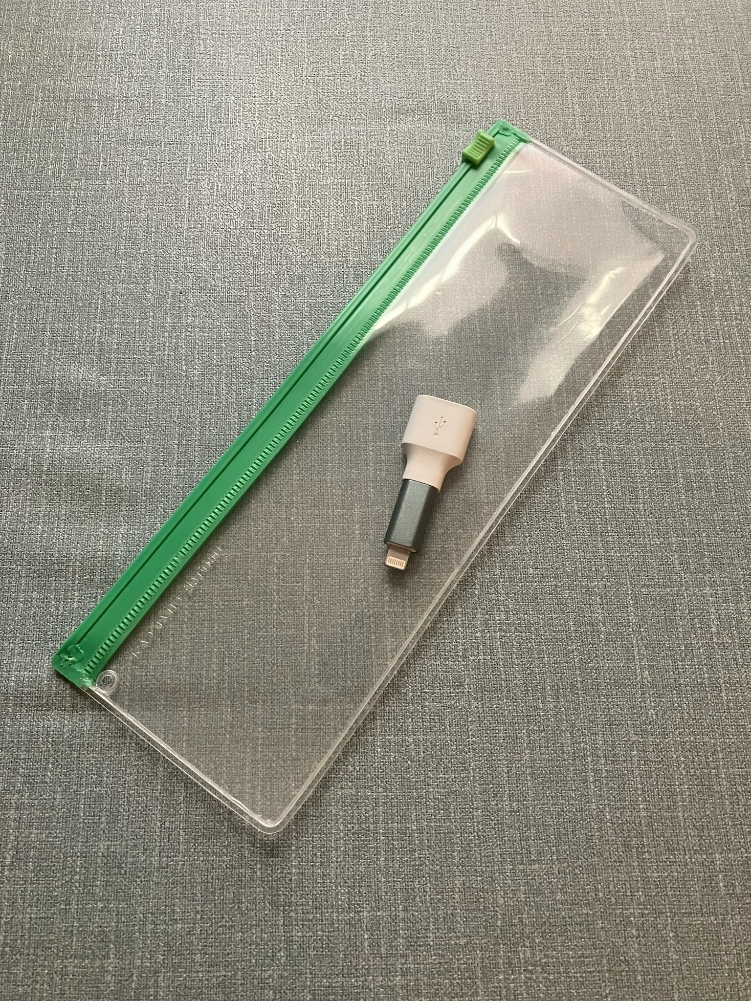 Pochette transparente avec une fermeture éclair verte et un stylo blanc