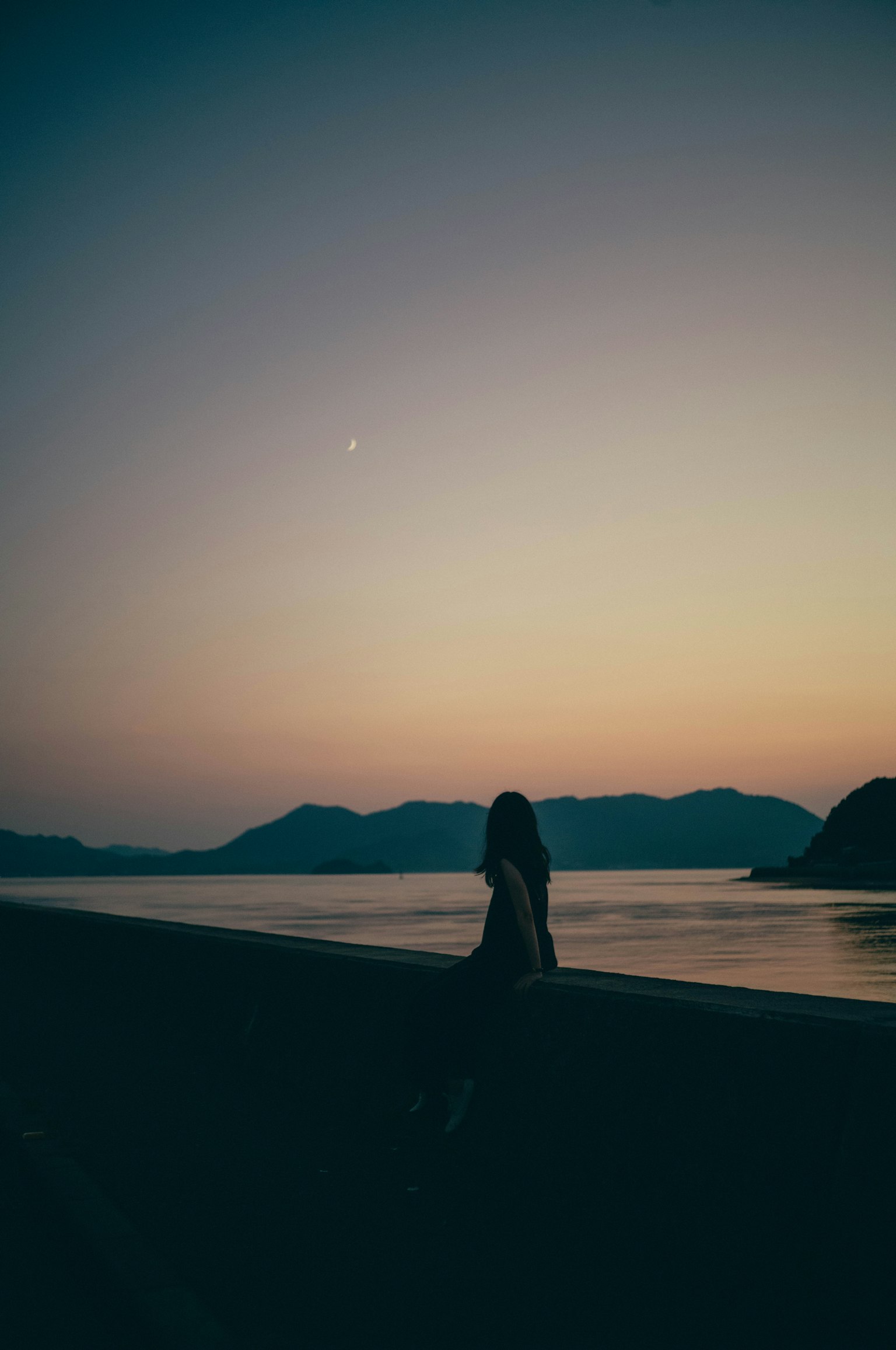 Silhouette di una donna seduta sulla tranquilla spiaggia al tramonto