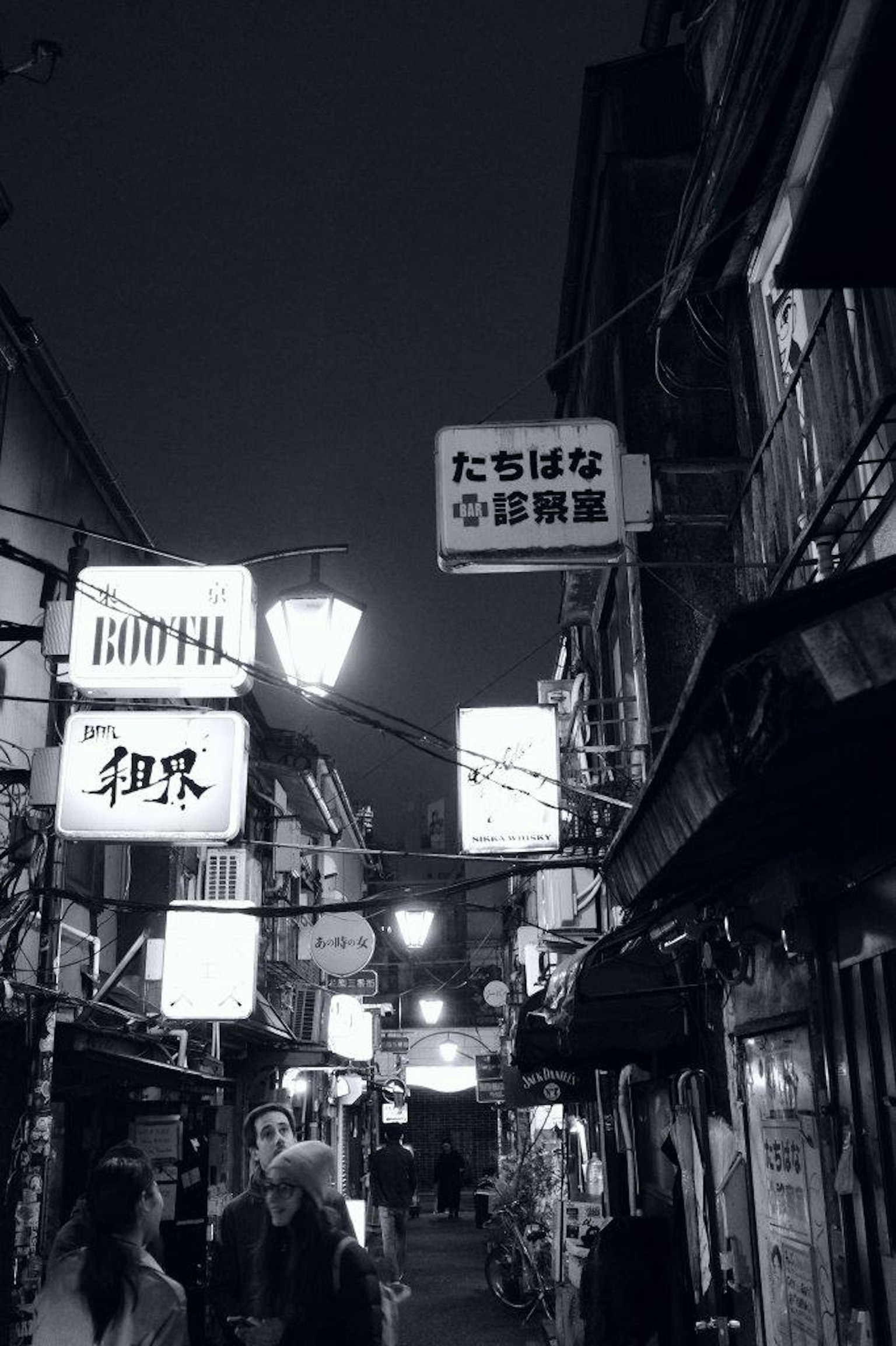 ถนนแคบในเวลากลางคืนที่มีป้ายร้านอาหารและโคมไฟถนน