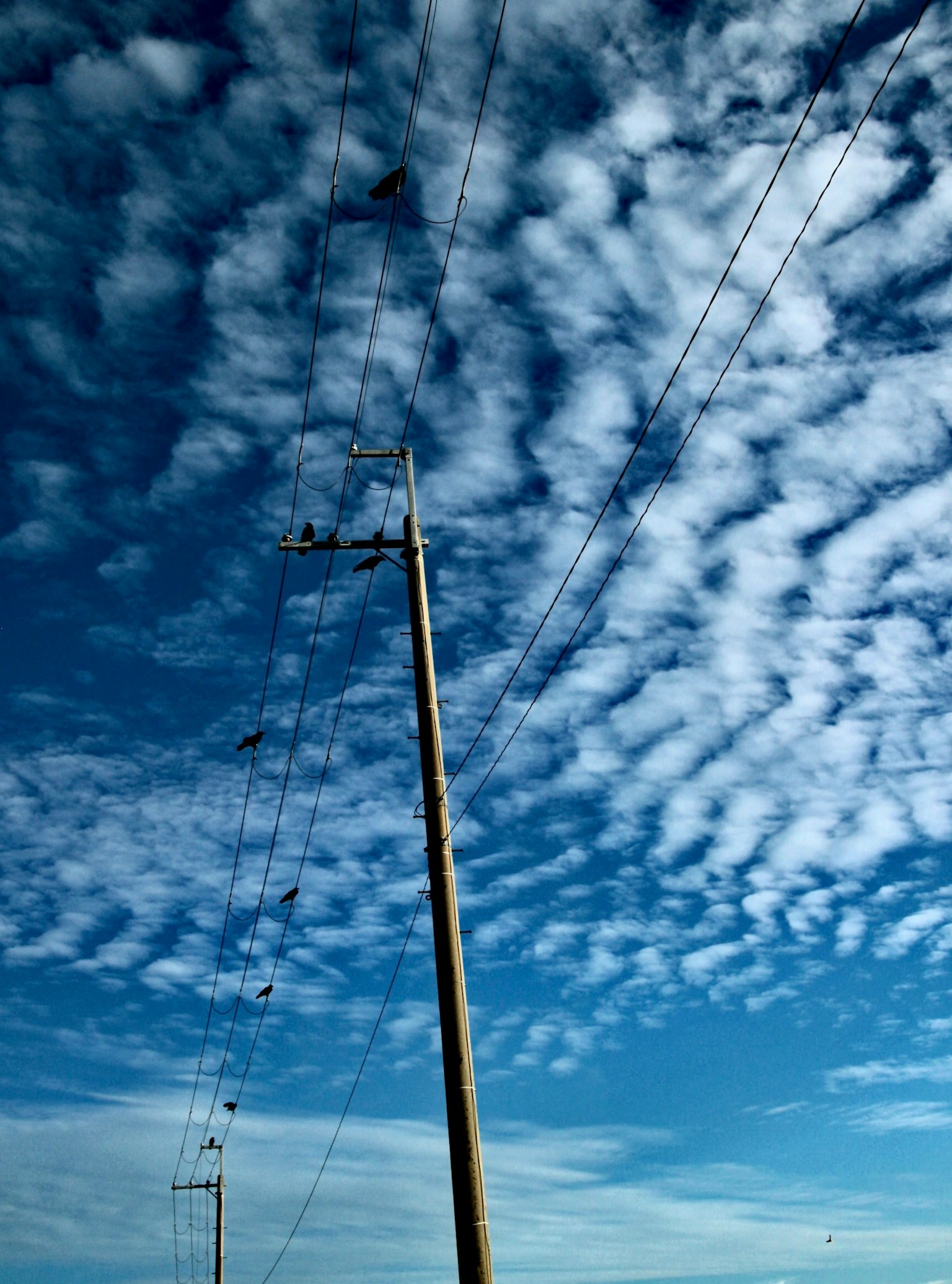Eine Landschaft mit einem Strommast vor einem Hintergrund aus blauem Himmel und verstreuten Wolken