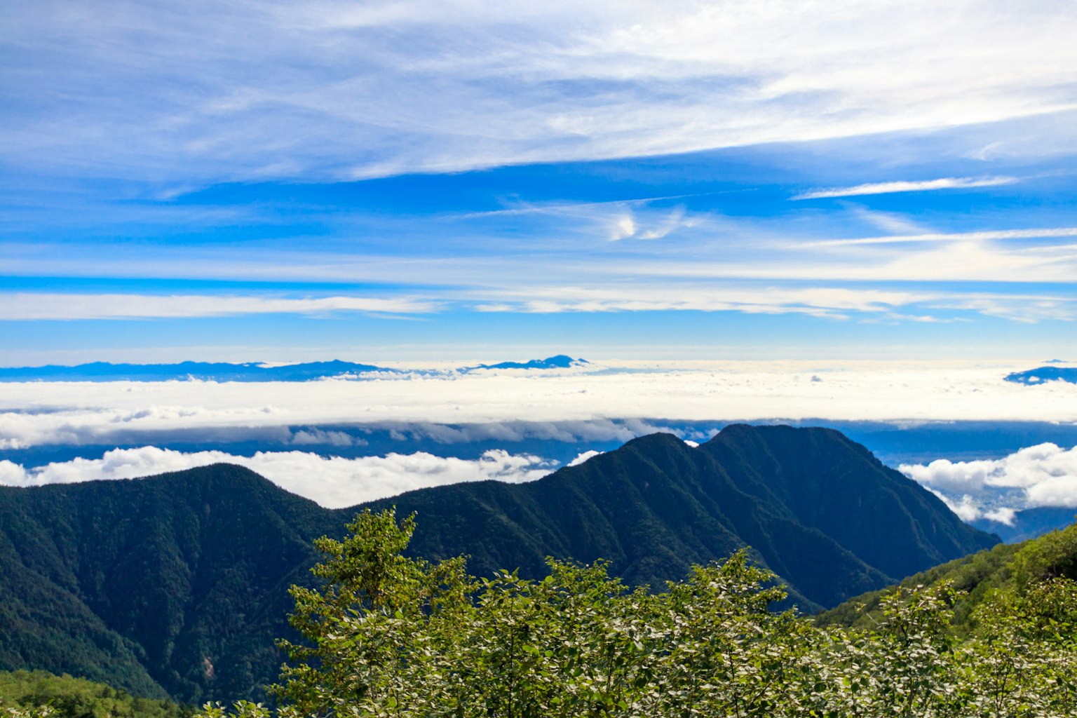 Paisaje montañoso rodeado de cielo azul y mar de nubes