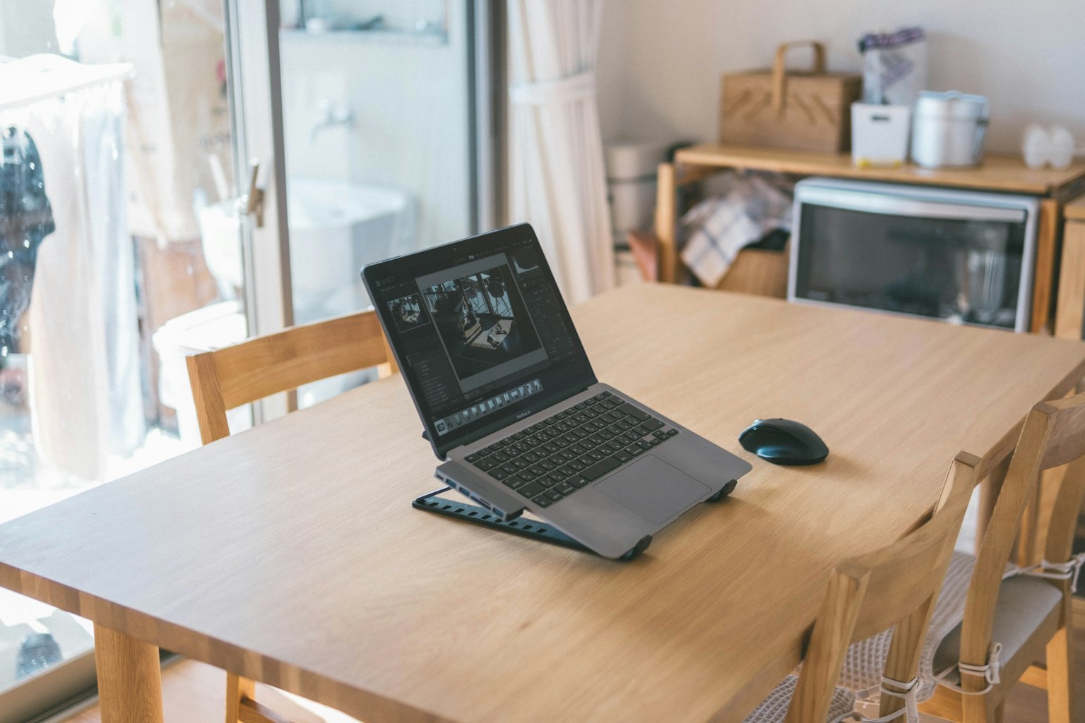 Gambar laptop dan mouse di atas meja kayu dengan cahaya alami masuk dari jendela