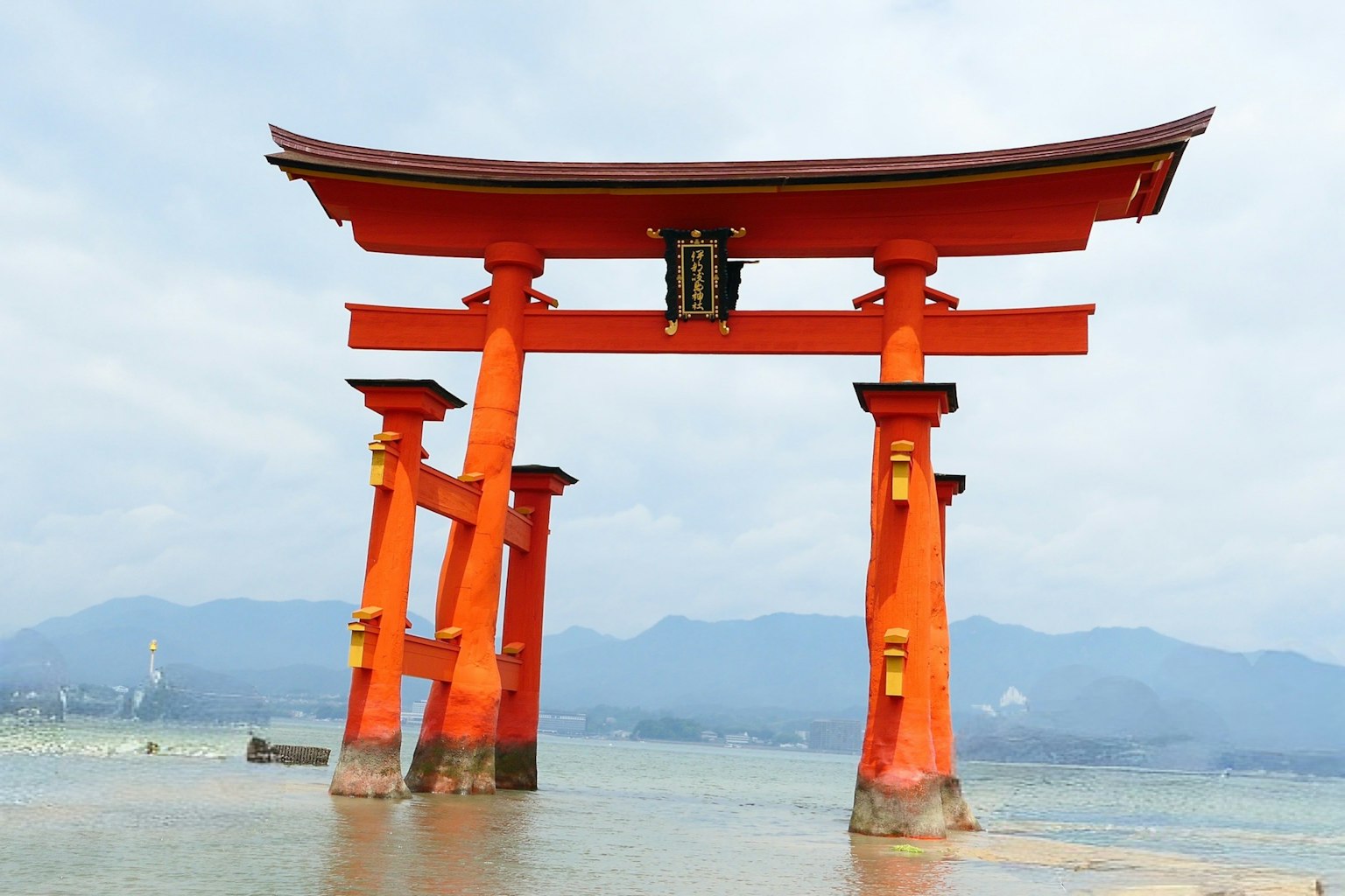 Ein rotes Torii-Tor steht im Wasser mit Bergen im Hintergrund