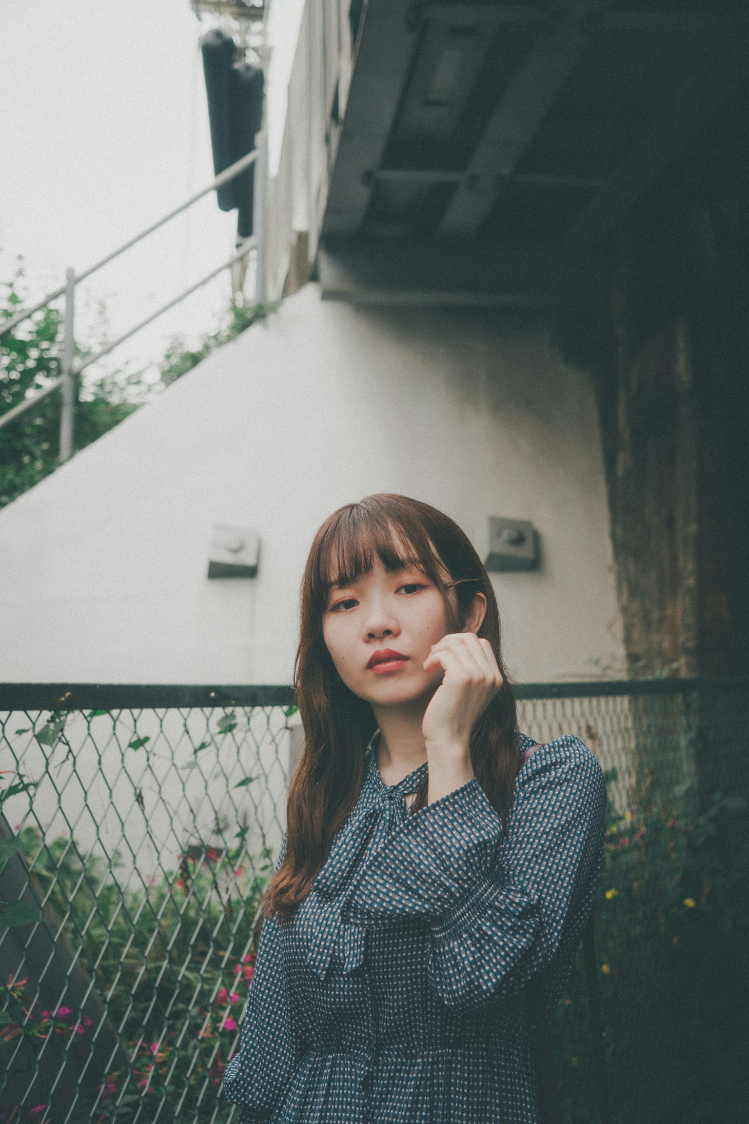 一位穿着灰色连衣裙的女性在户外摆姿势，背景有围栏和墙壁