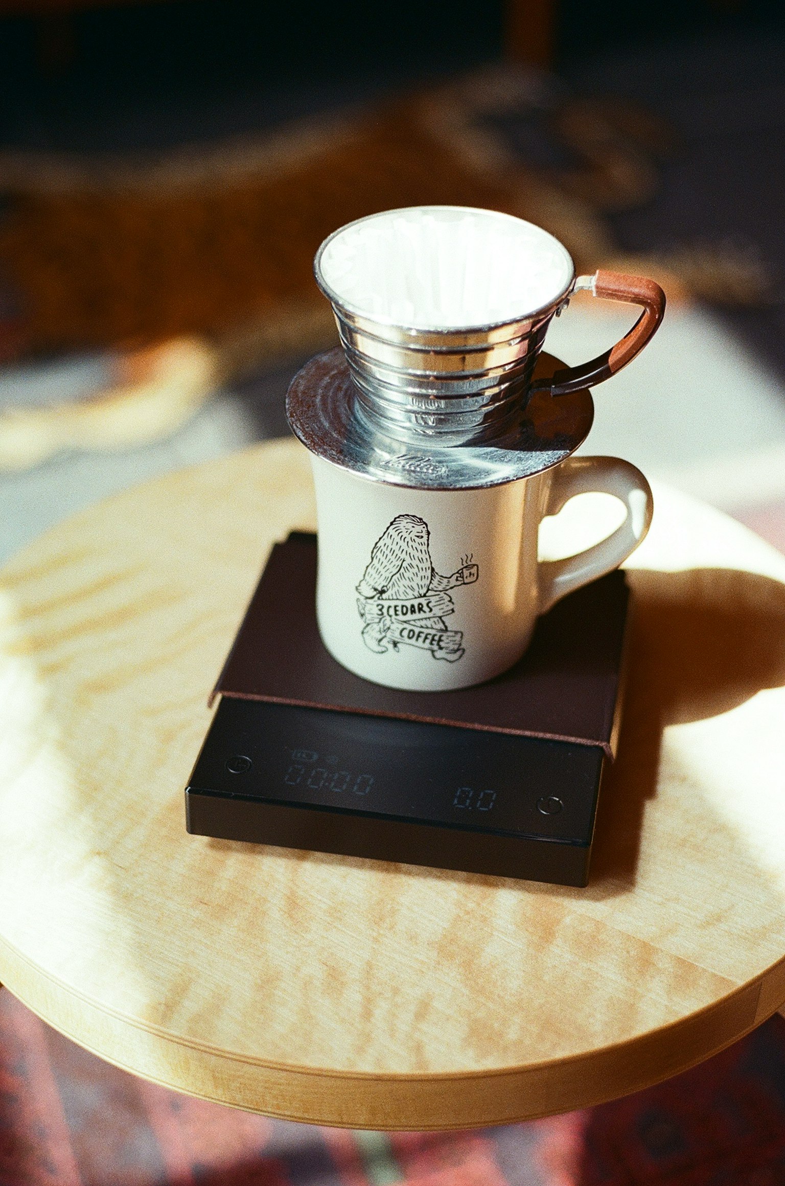 Imagen que muestra un conjunto de preparación de café con una taza blanca y un filtro de metal sobre una superficie de madera