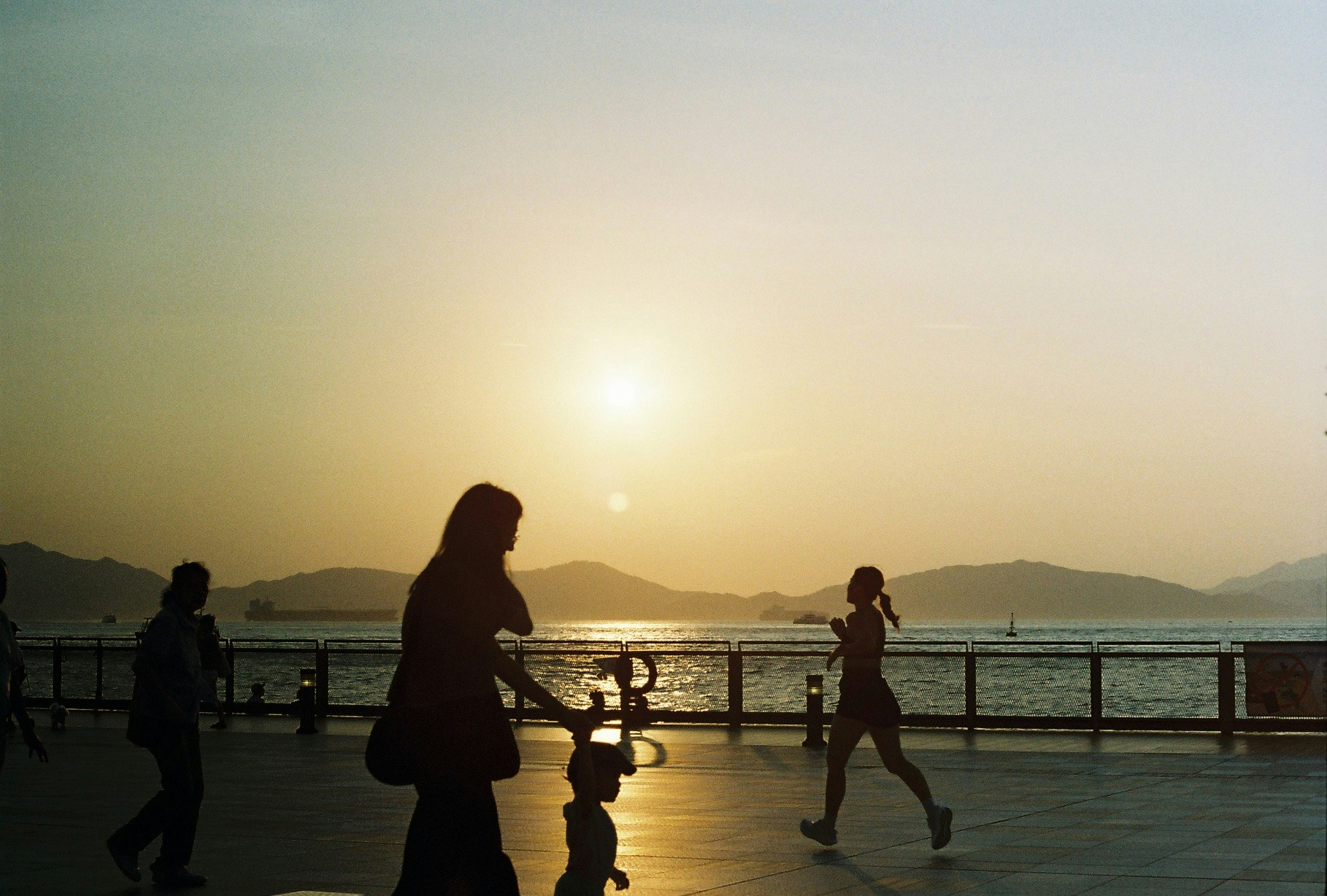 夕日に照らされた海辺の遊歩道を歩く親子