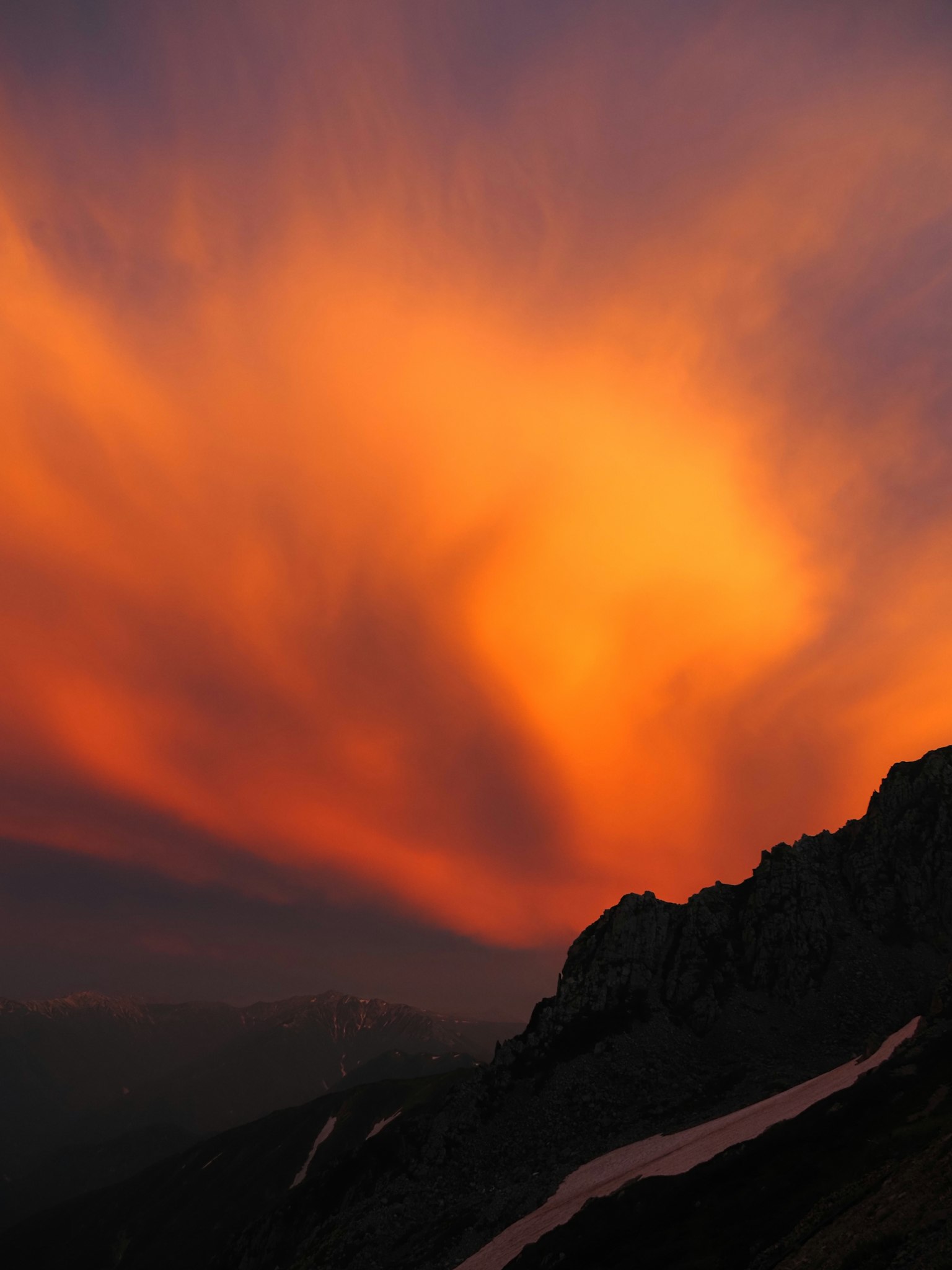 夕焼けのオレンジ色の雲が山の上に広がる美しい風景