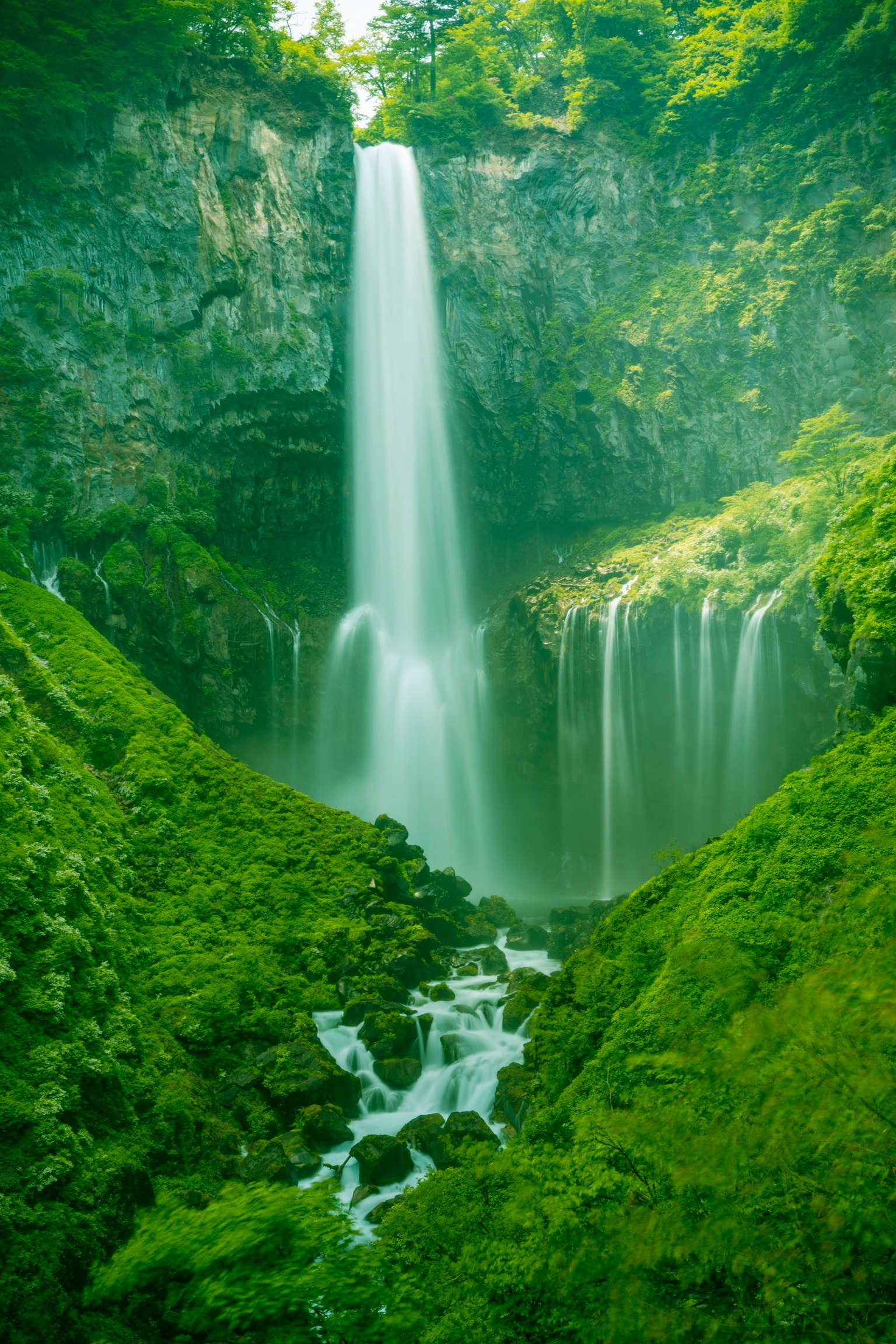 A beautiful landscape of a waterfall surrounded by greenery with a tall waterfall cascading down