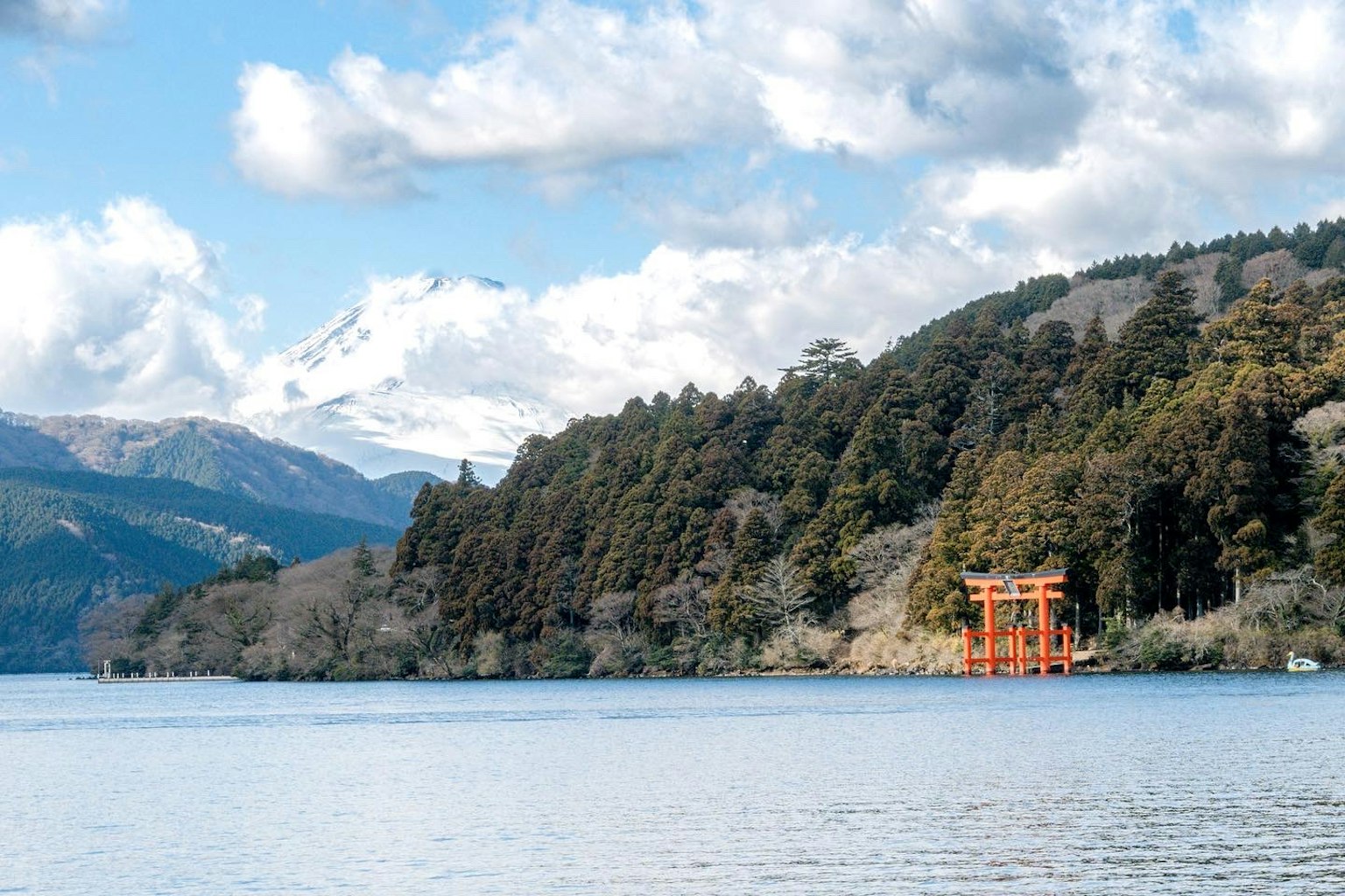 A scenic view of a lake with a red torii gate and mountains in the background