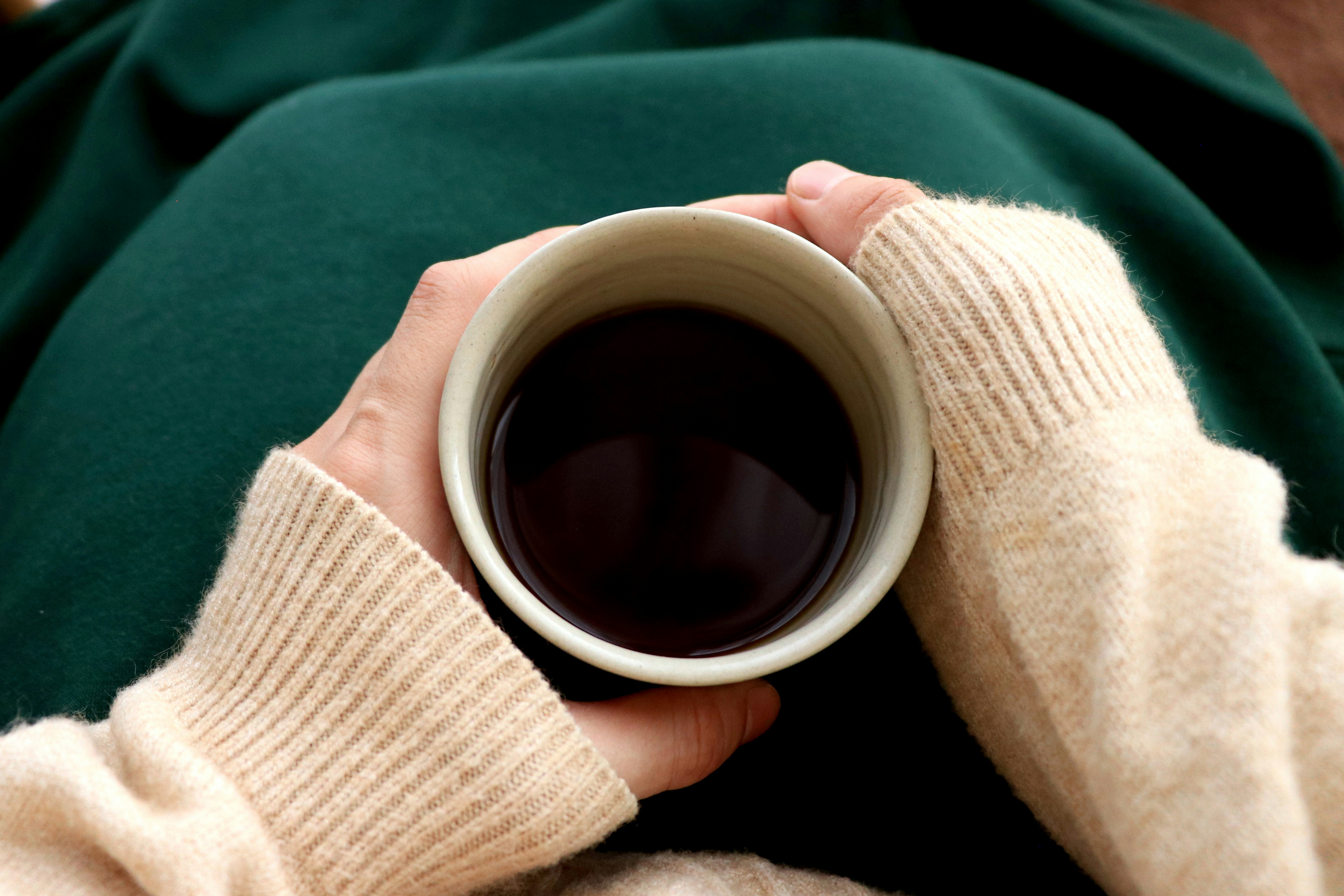 Una taza de bebida caliente sostenida por una mano envuelta en una manta