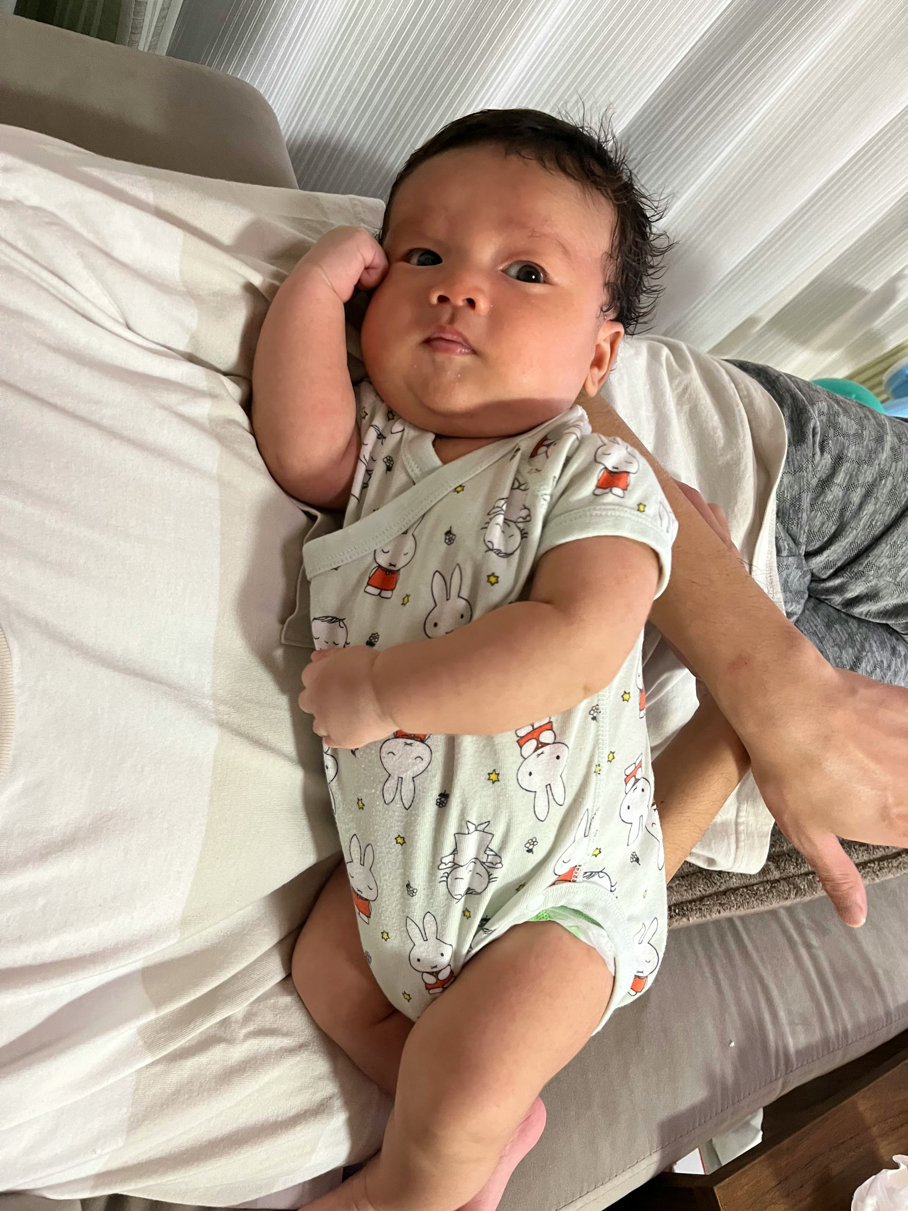 baby lying on a bed being held and looking up