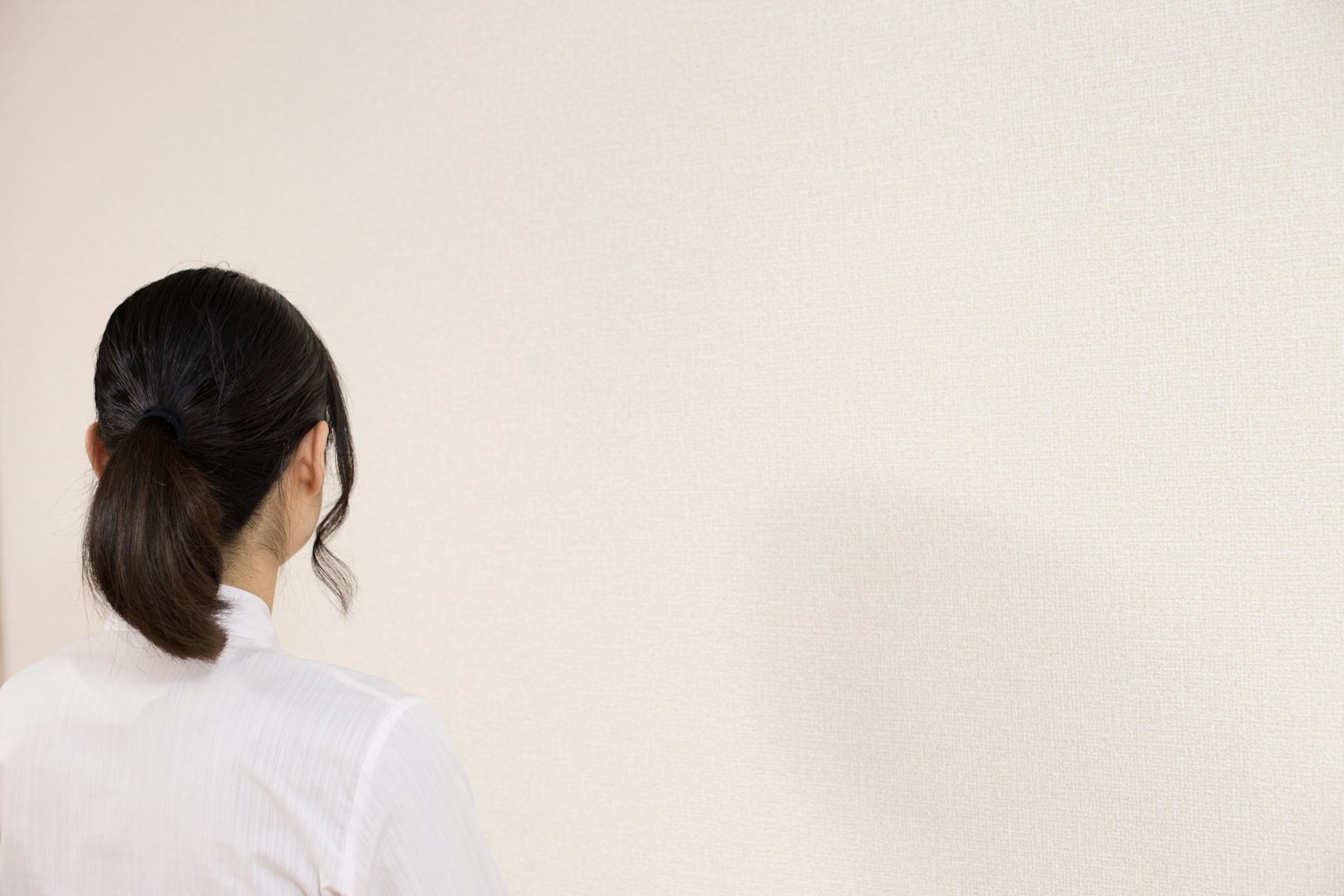 Một người phụ nữ nhìn từ phía sau đối diện với một bức tường trắng đơn giản