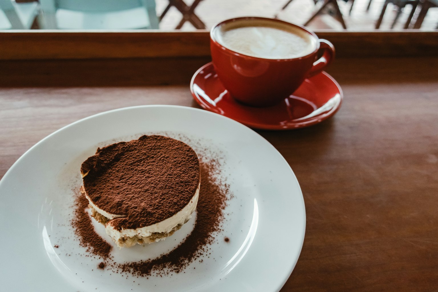 Tiramisú cubierto de cacao servido con una taza de cappuccino