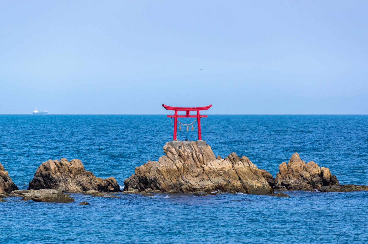 Torii rojo en un afloramiento rocoso en el océano azul