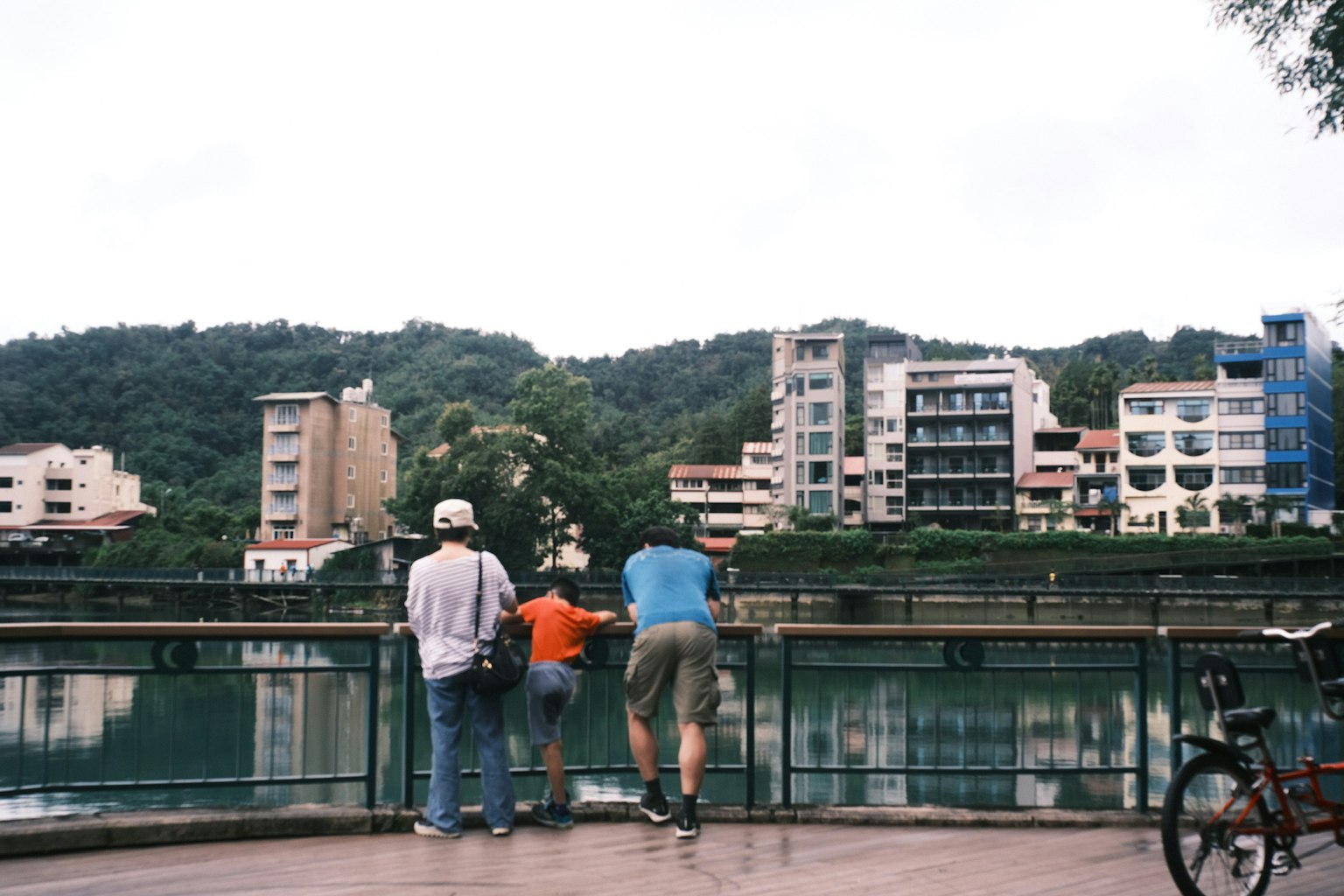 Family enjoying the view by the river with modern buildings and green hills in the background
