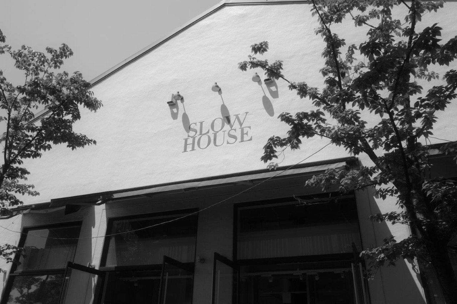 Extérieur d'un bâtiment avec le logo de Slow House entouré d'arbres