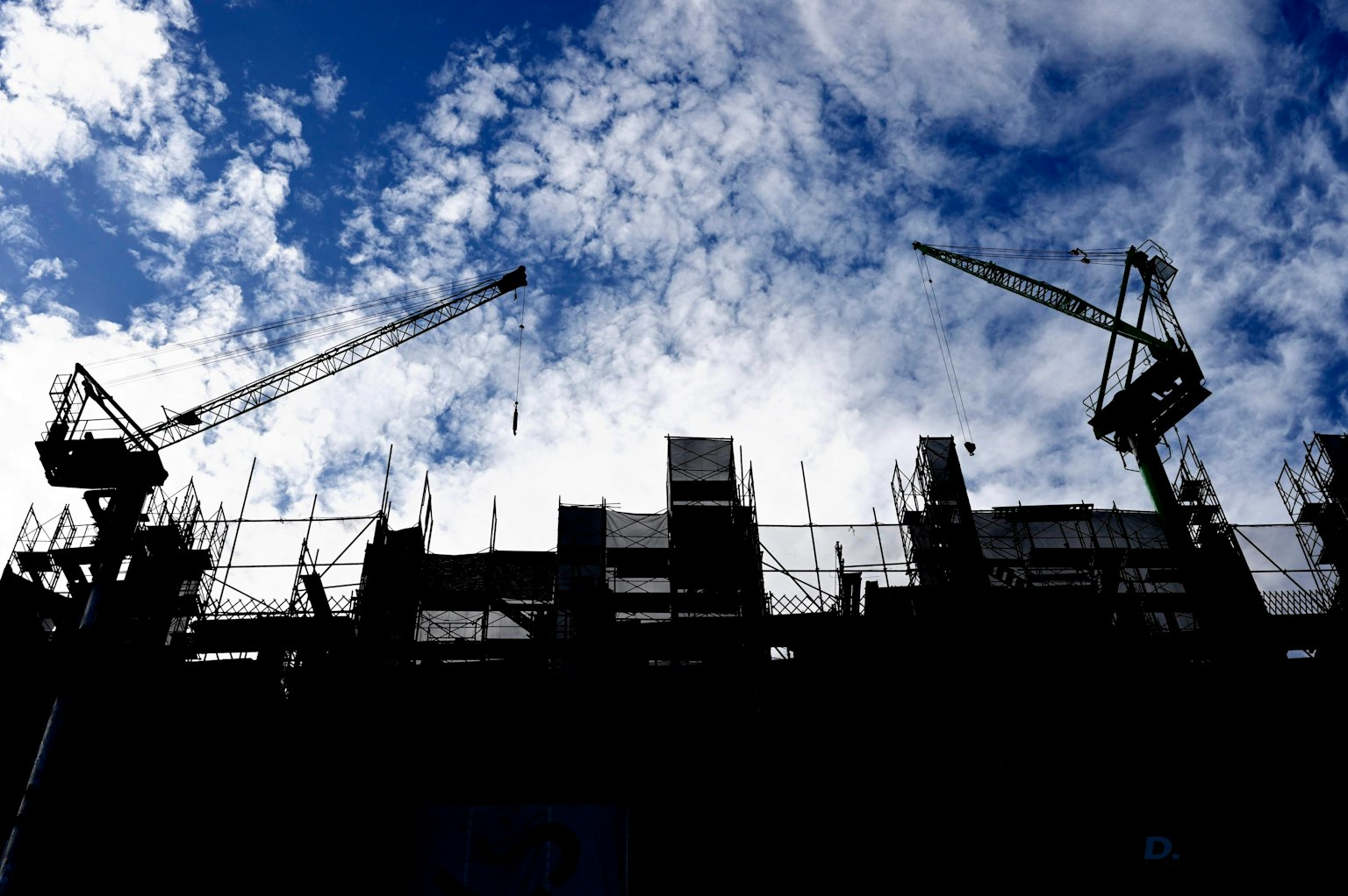 Silueta de un sitio de construcción con grúas contra un cielo azul y nubes