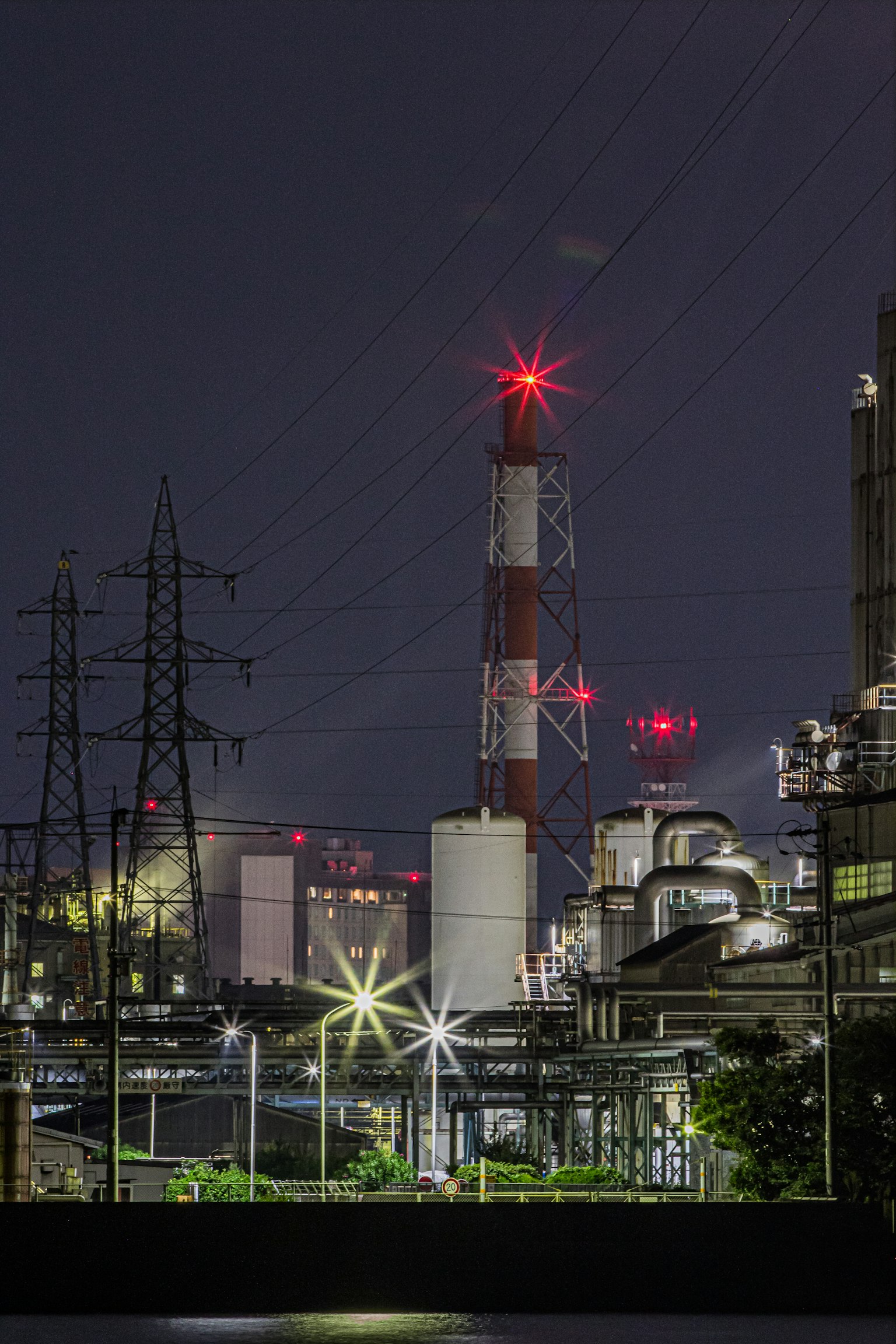 Paisaje industrial nocturno con una chimenea y líneas eléctricas
