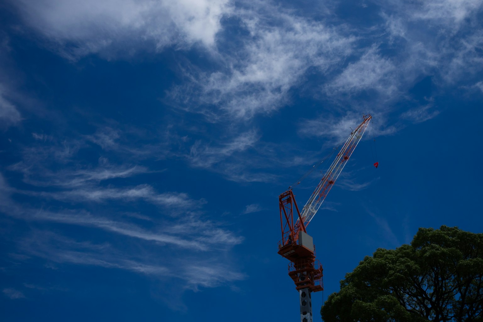 Una grúa roja contra un cielo azul con nubes blancas