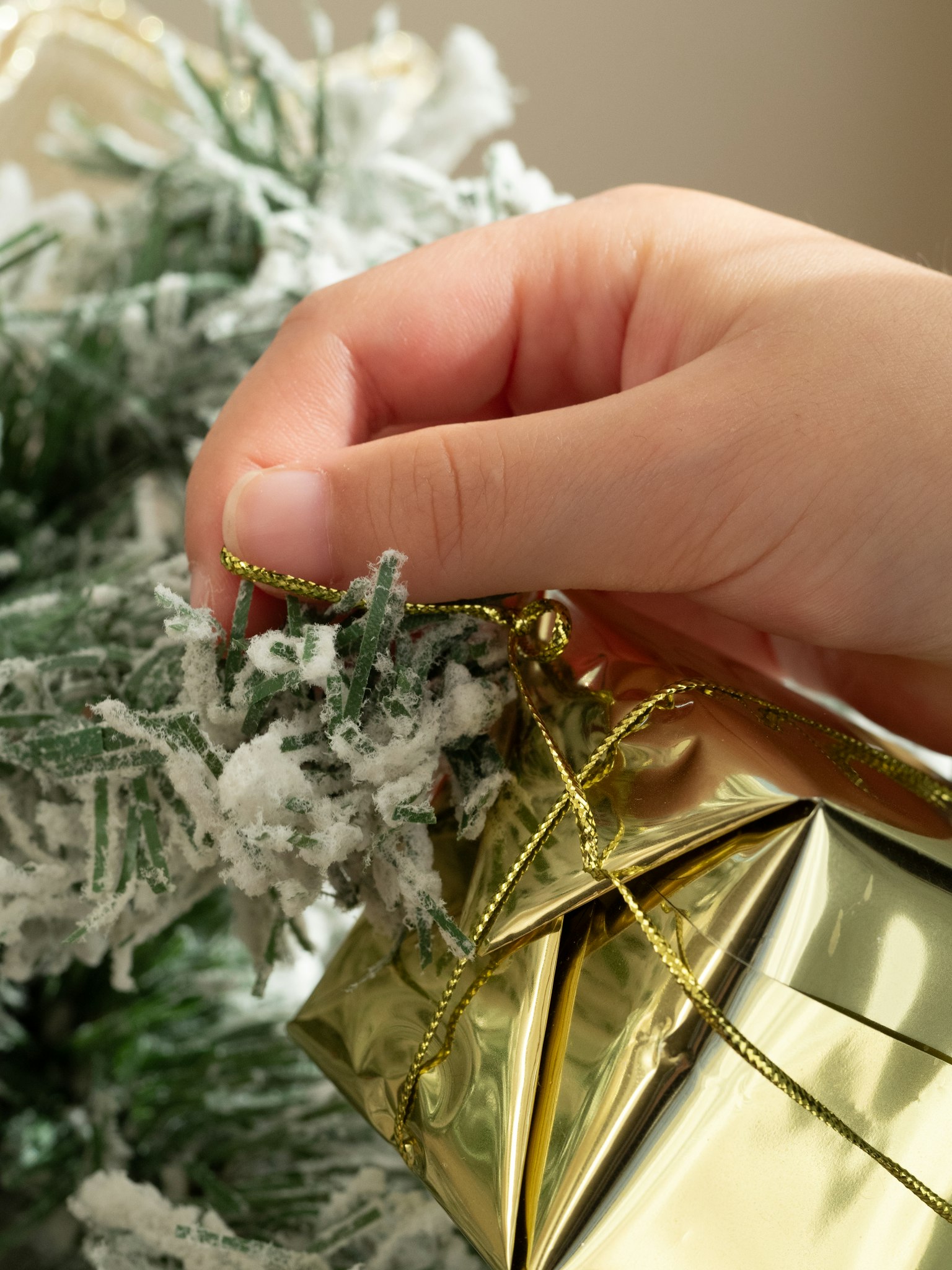 Hand holding a golden gift near a snowy Christmas tree