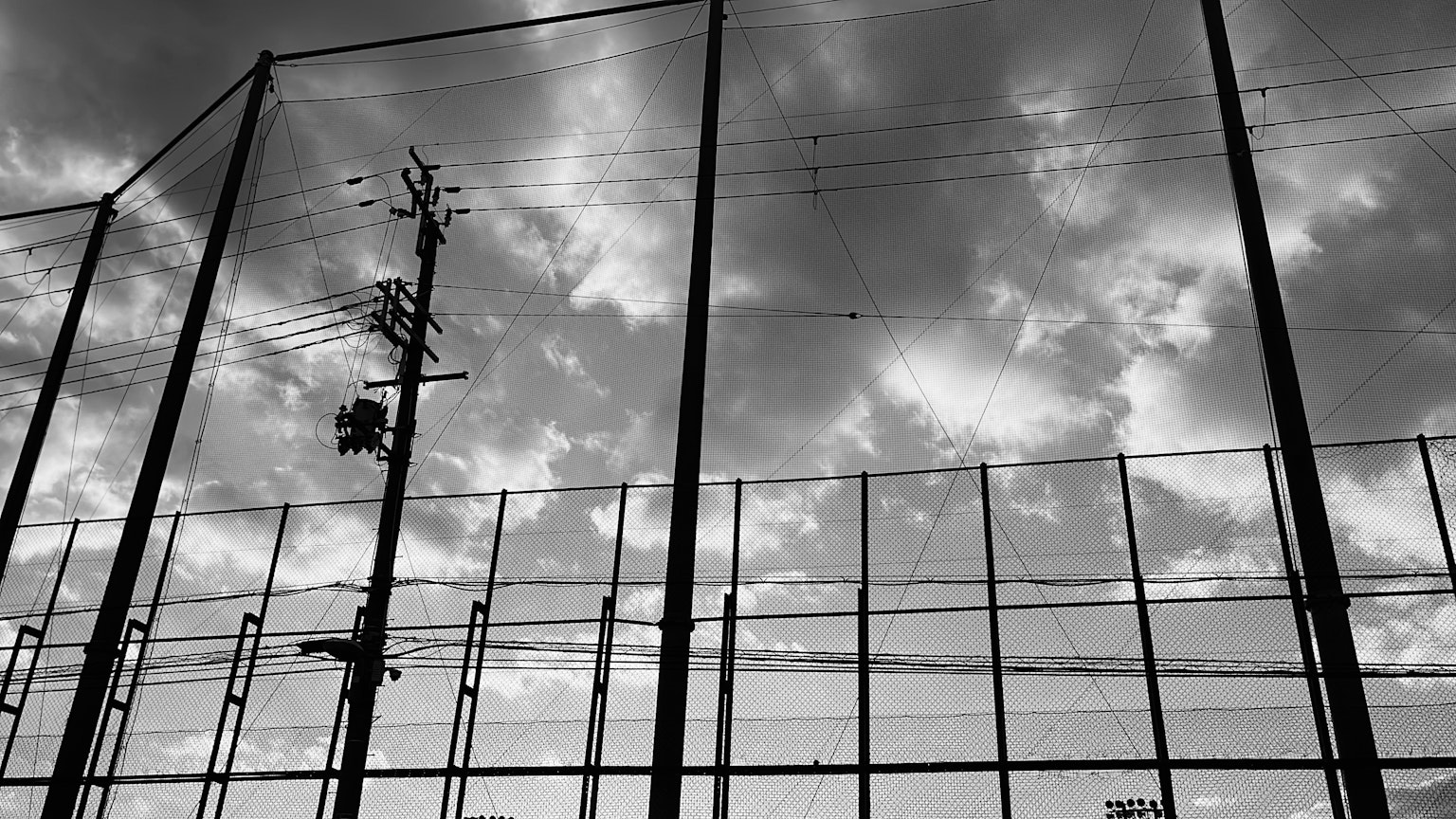 Baseball field fence and utility pole under a black and white sky