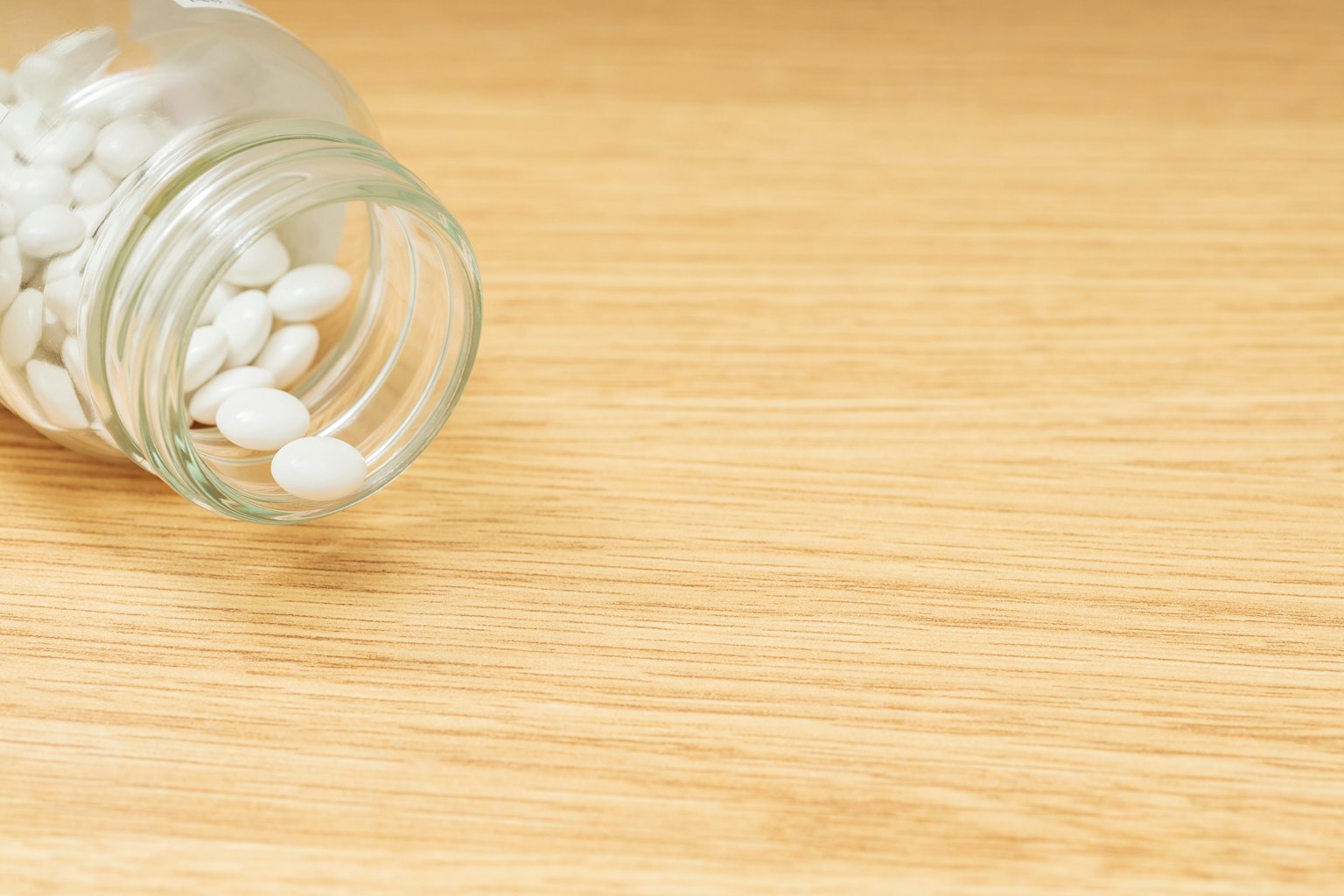 White pills scattered around an overturned glass jar