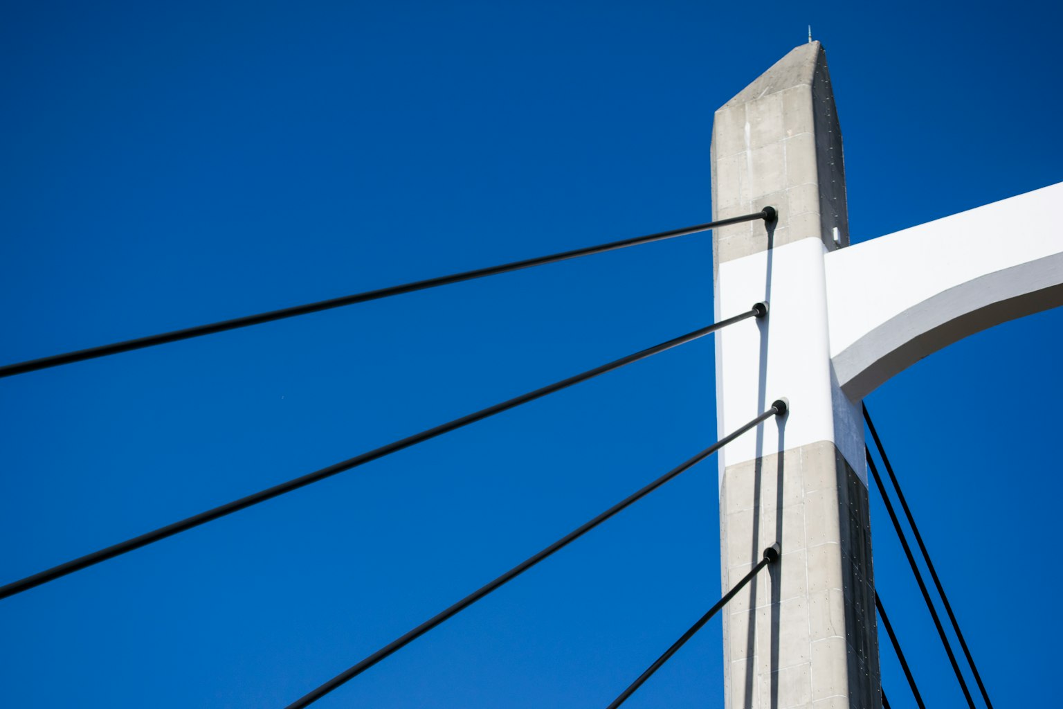 Weißer Brückenpfeiler und Kabel vor blauem Himmel