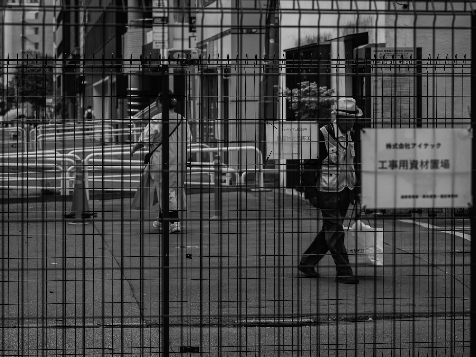 Un lavoratore e un passante che camminano davanti a una recinzione di cantiere