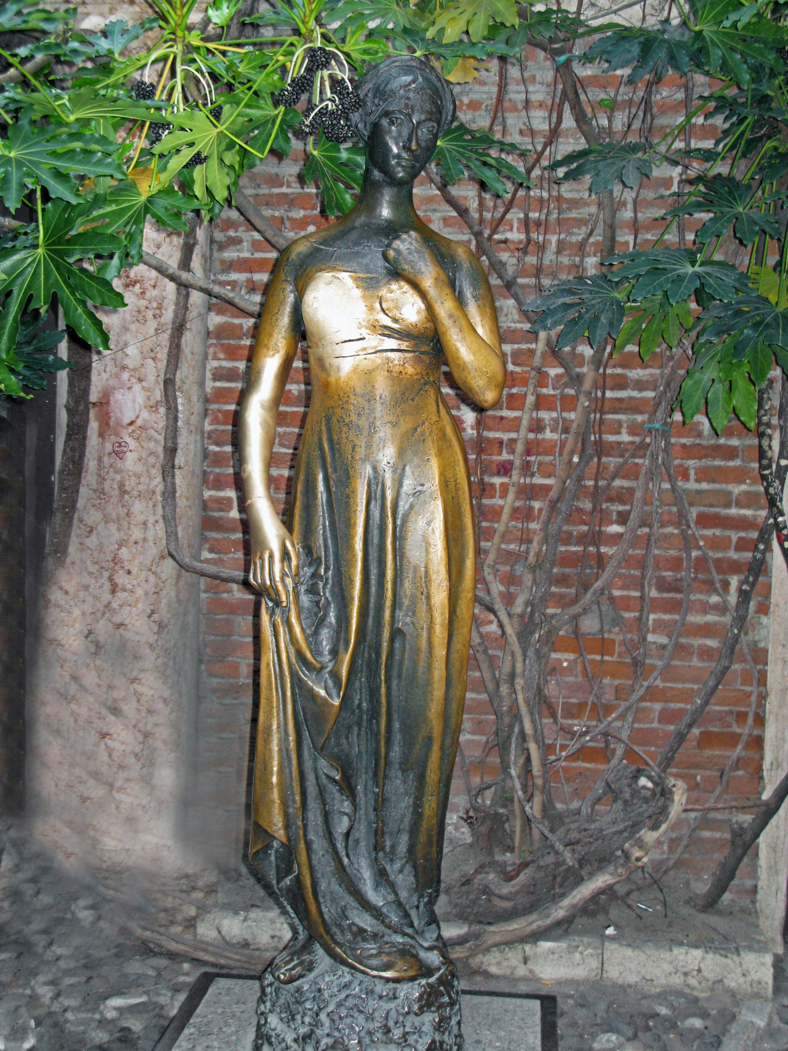 Eine elegante Bronzestatue in einem Garten mit einem goldenen Kleid