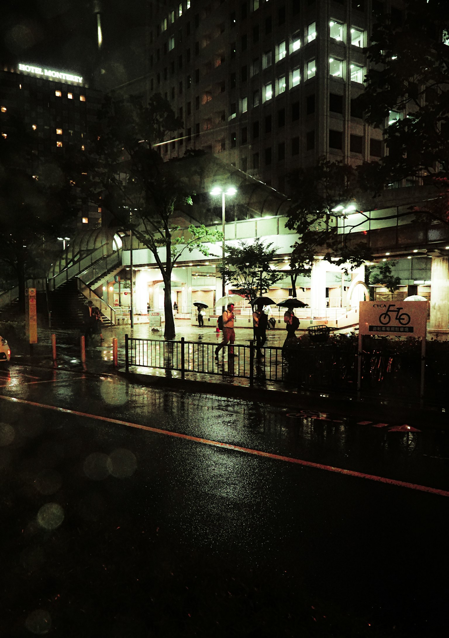 夜晚城市景觀，撐著雨傘的人和被雨水浸濕的街道