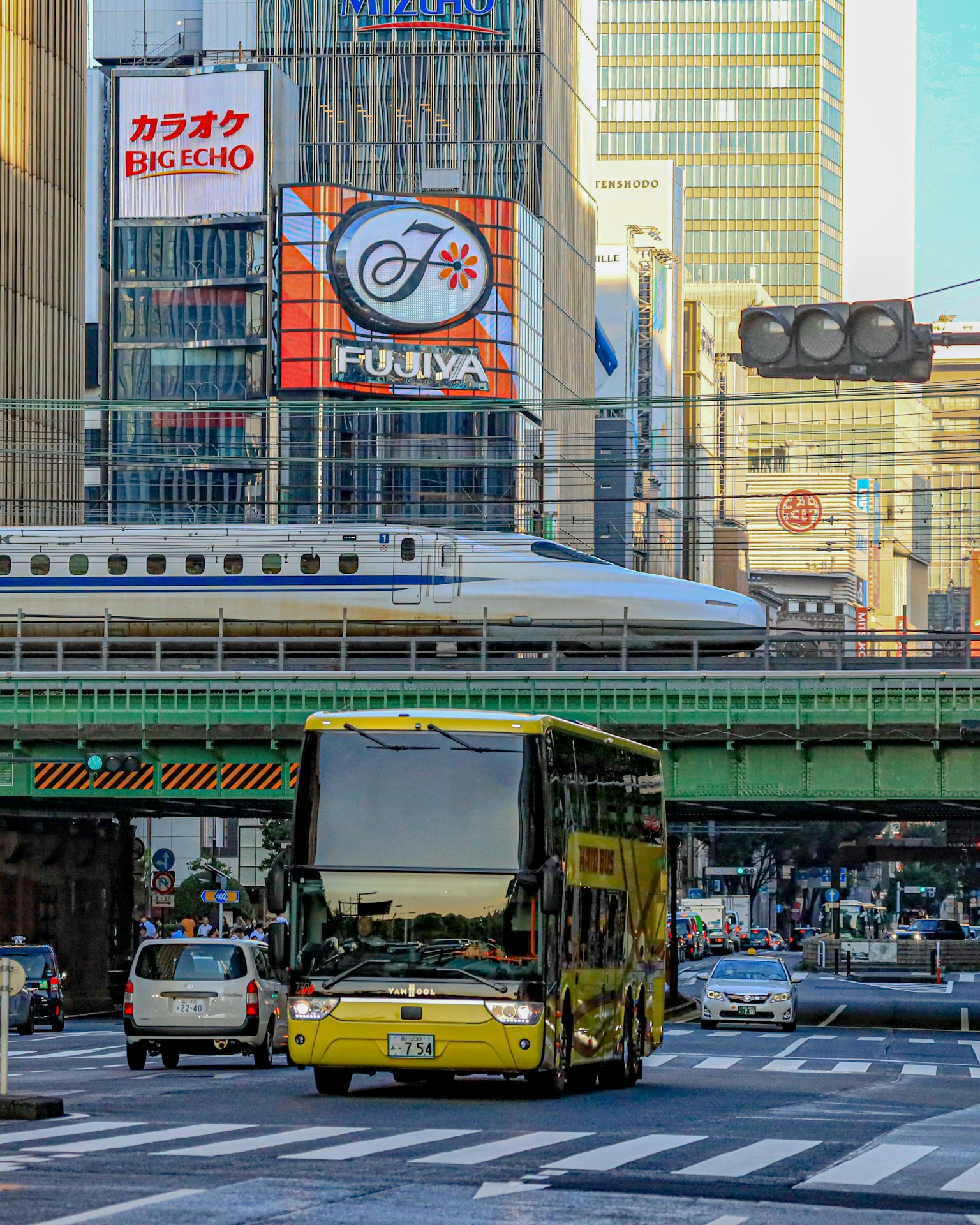 Ein gelber Doppeldeckerbus in einer belebten Stadtszene mit einem Shinkansen-Zug