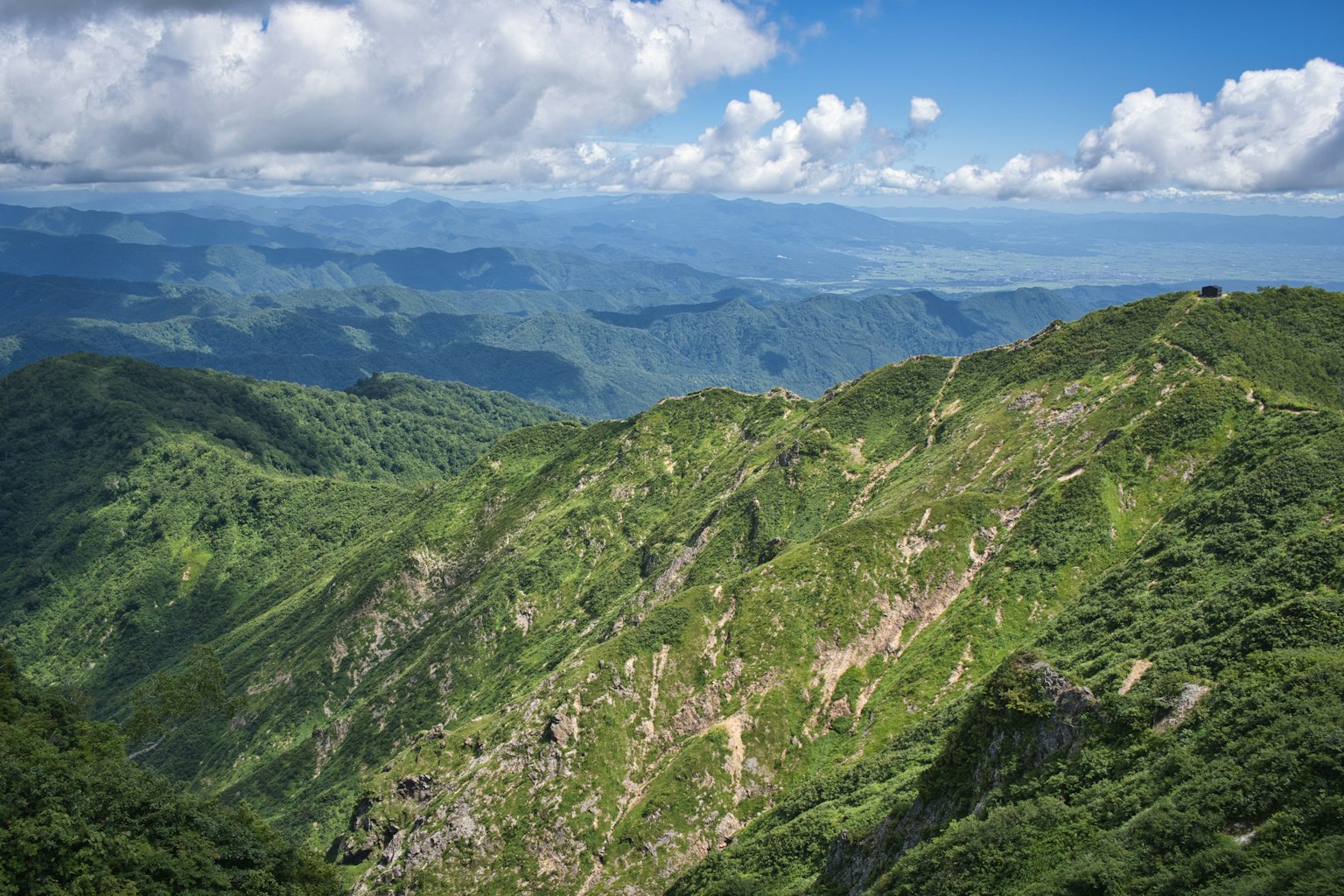 Montañas verdes bajo un cielo azul con nubes blancas