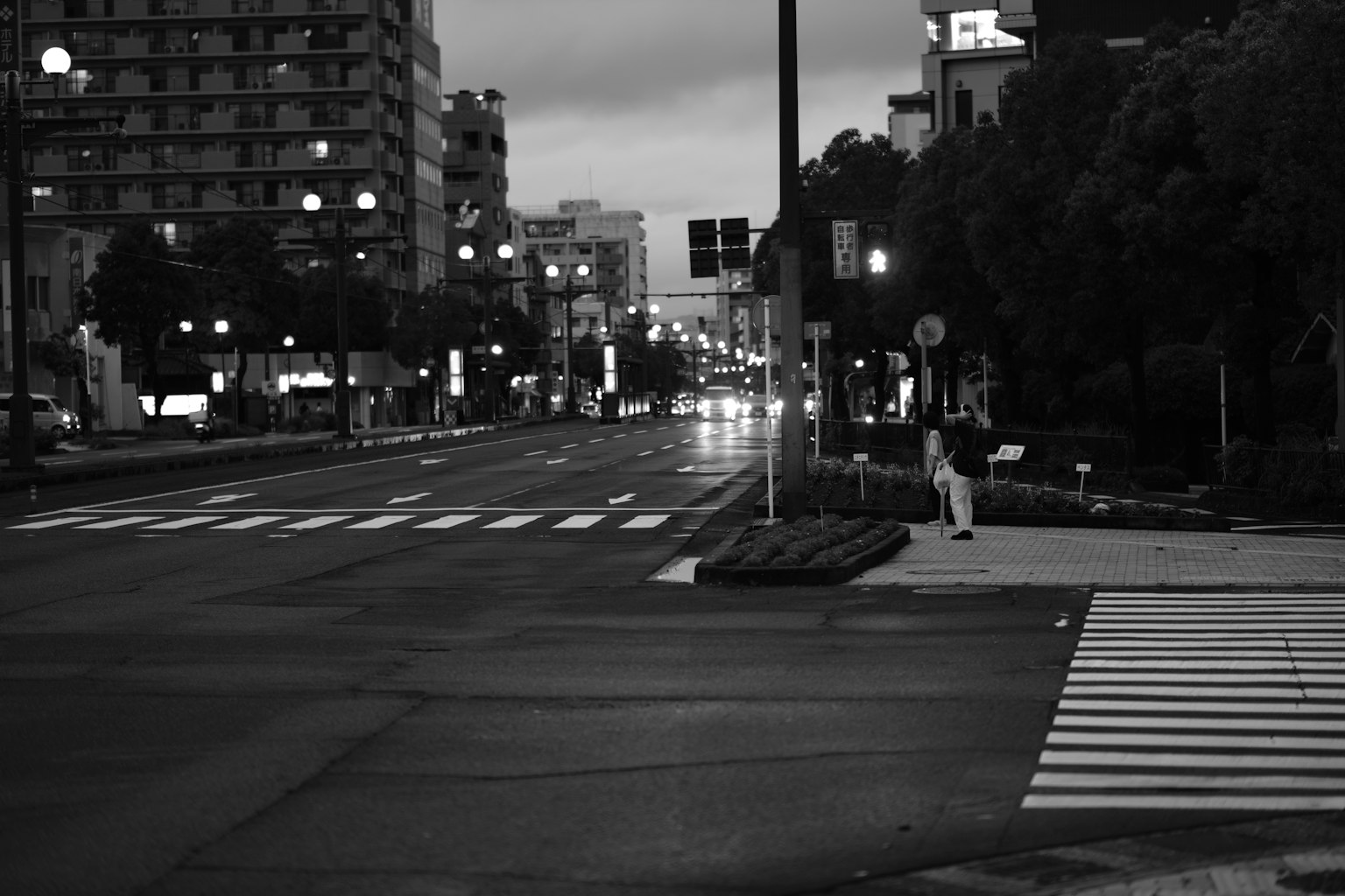 一个人在夜间街道交叉口站着，周围有照明建筑