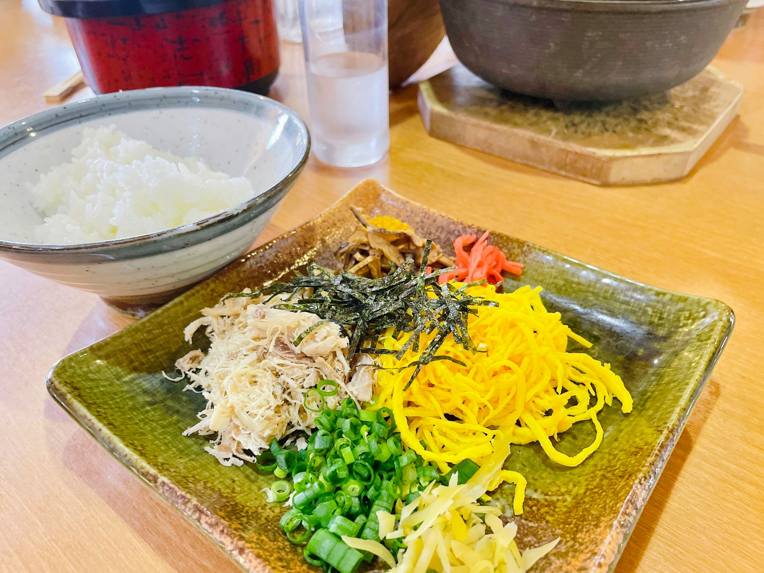 Piring dengan bahan berwarna-warni termasuk ayam suwir, telur kuning, dan daun bawang di samping mangkuk nasi putih