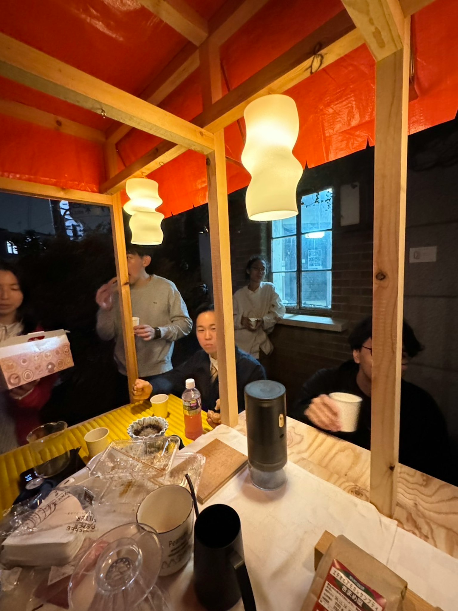 室内摊位中人们手持饮品，温暖的灯光