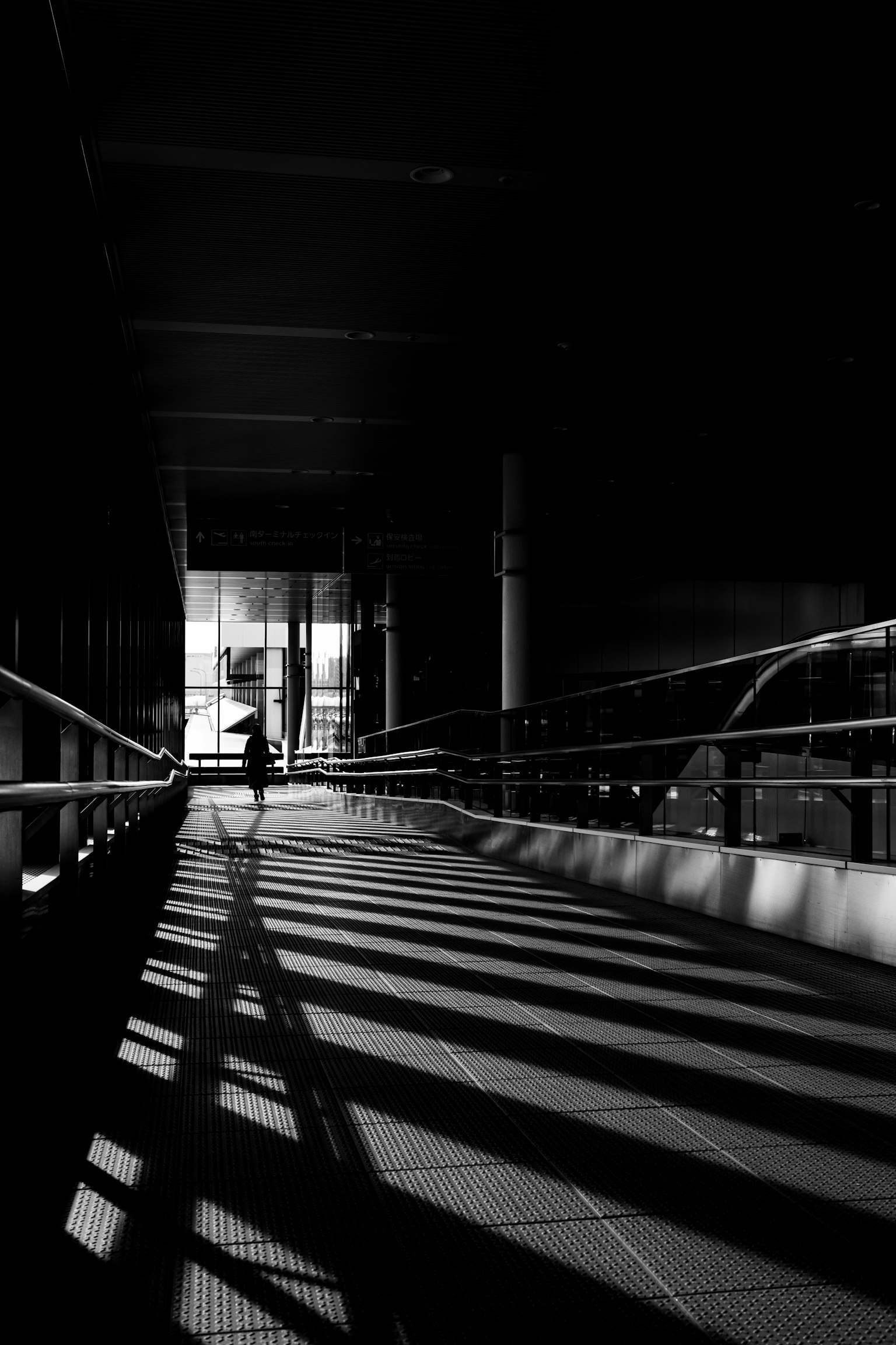 Foto en blanco y negro de una figura caminando en un pasillo oscuro con largas sombras