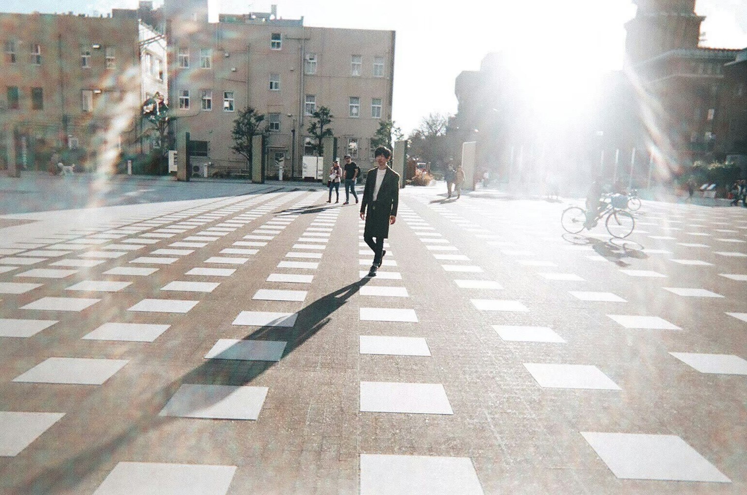 Una persona caminando bajo la luz brillante en una plaza con azulejos blancos