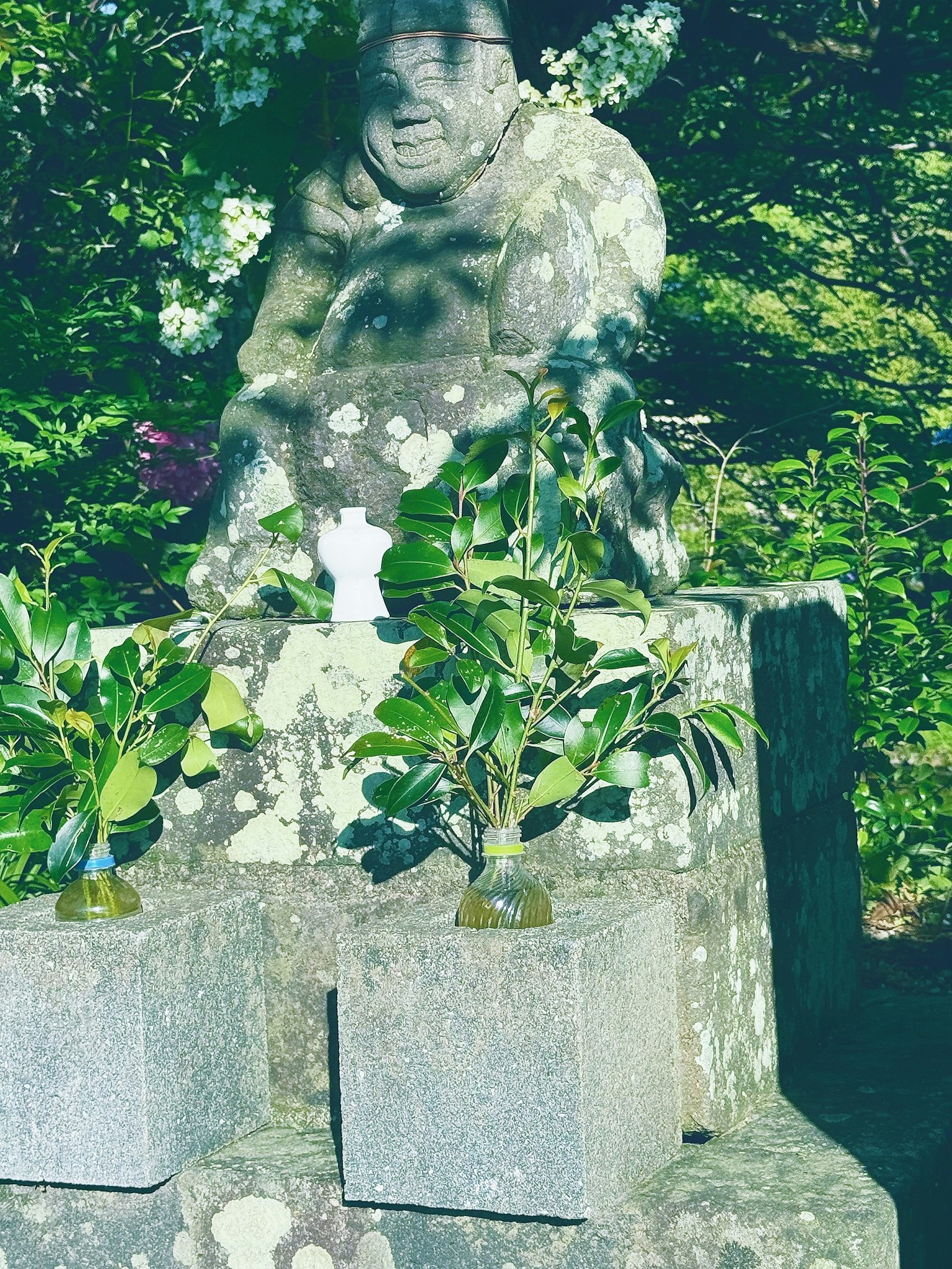 Statua in pietra antica circondata da vegetazione con piante accanto