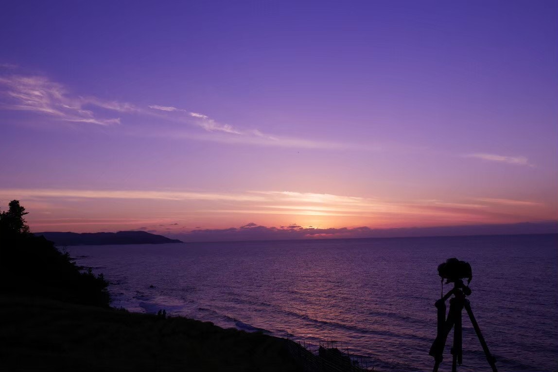 夕暮れの海辺で三脚を構える人物