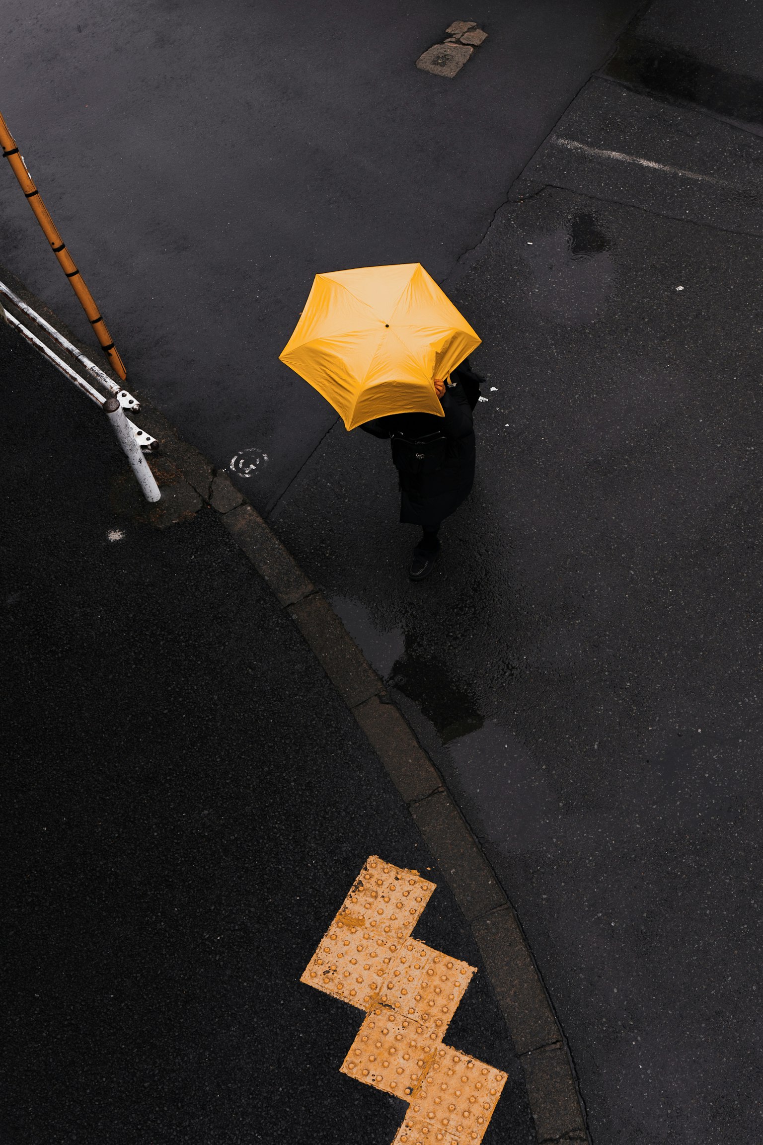 一個人在濕漉漉的道路上走著，手裡拿著一把黃色的雨傘