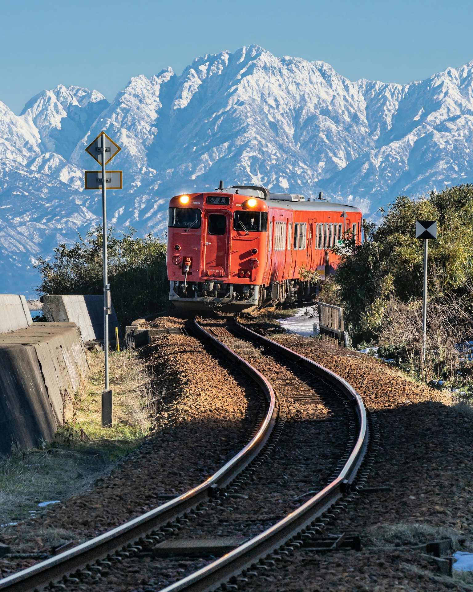 Treno rosso che viaggia su binari curvi con montagne innevate sullo sfondo