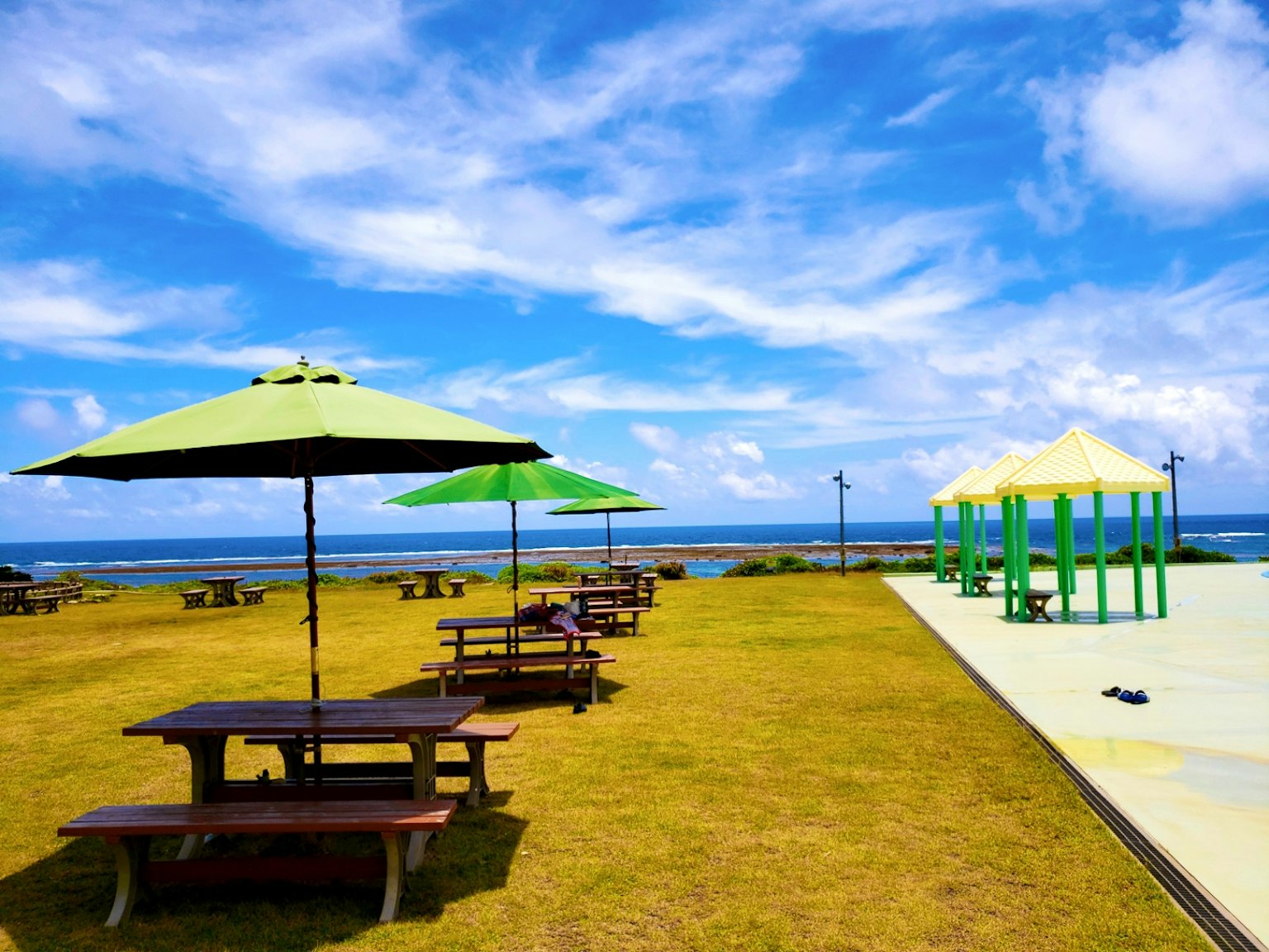 Cảnh bãi biển với ô xanh và bàn picnic dưới bầu trời xanh và đại dương