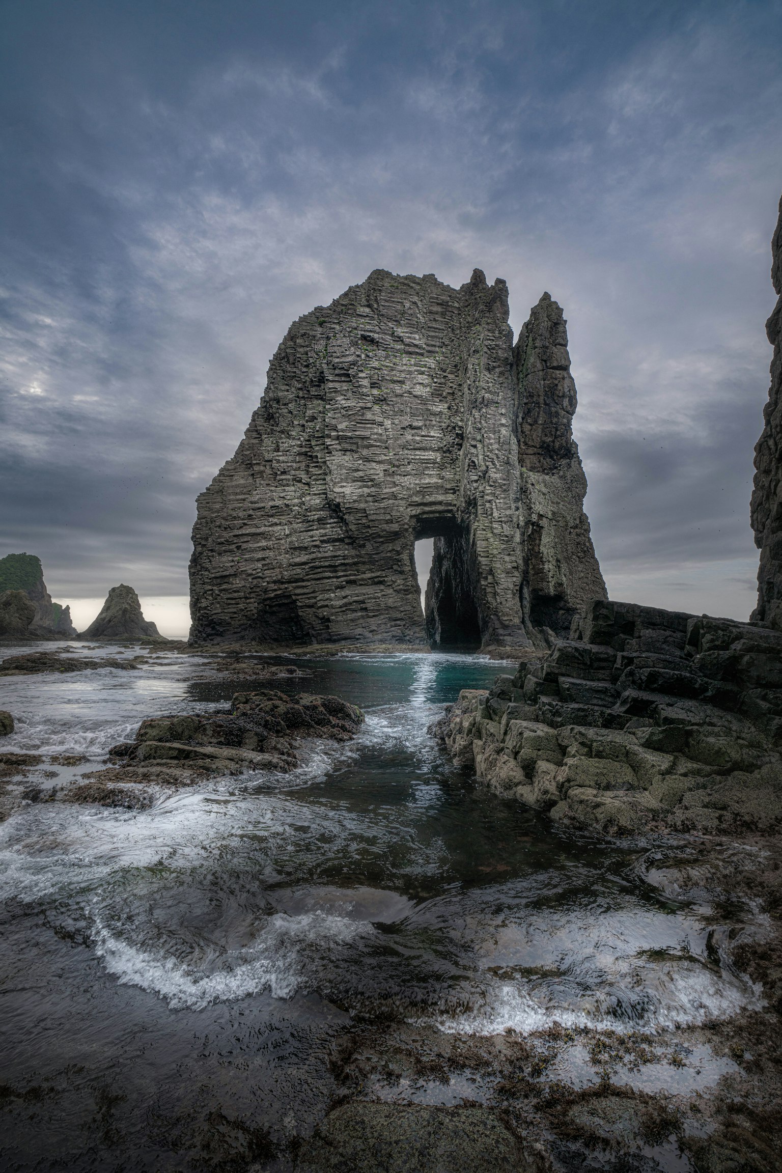 Coastal rock arch with waves and dramatic sky