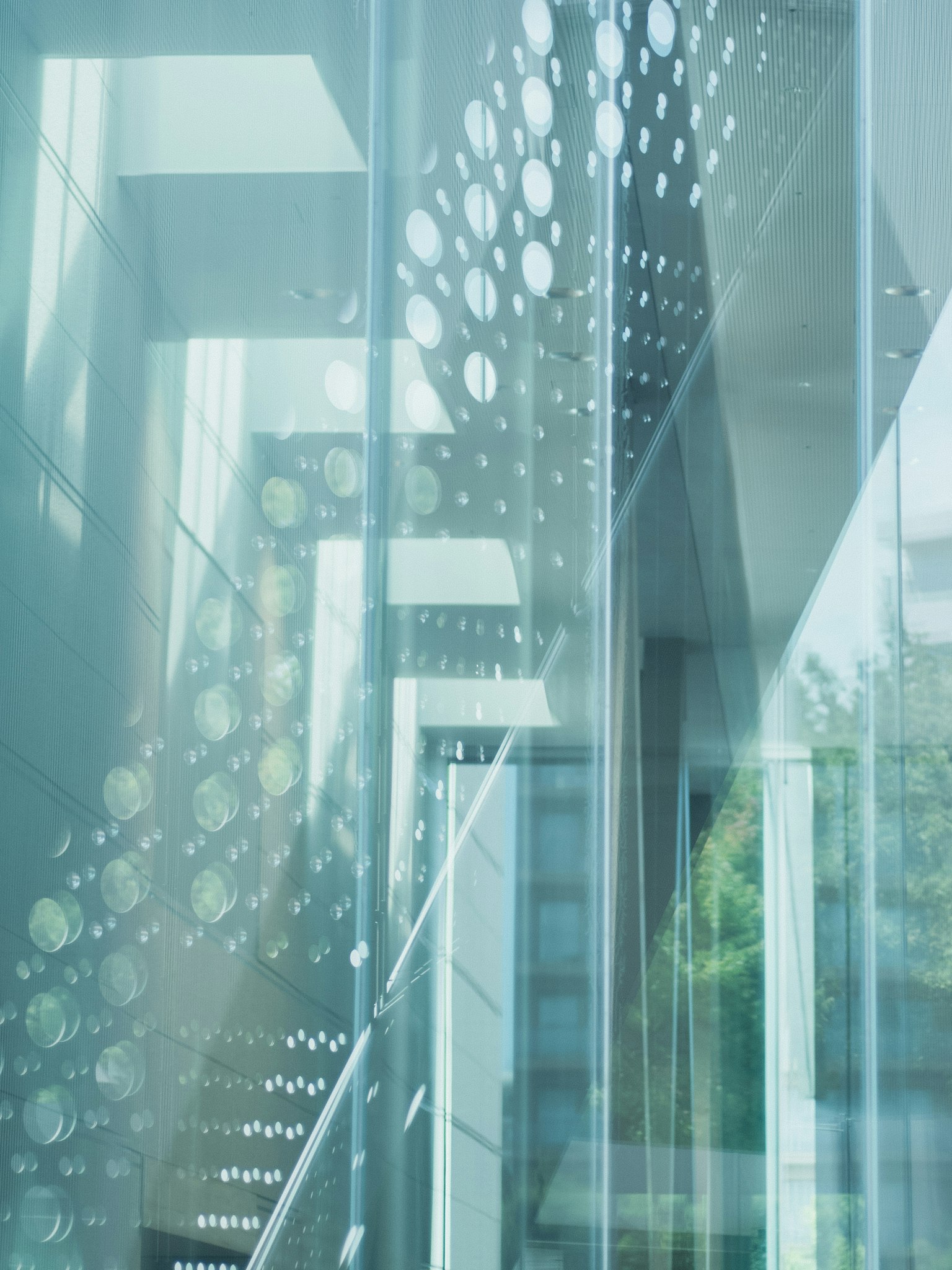 Interior de un edificio moderno con escalera de vidrio transparente y paneles perforados únicos